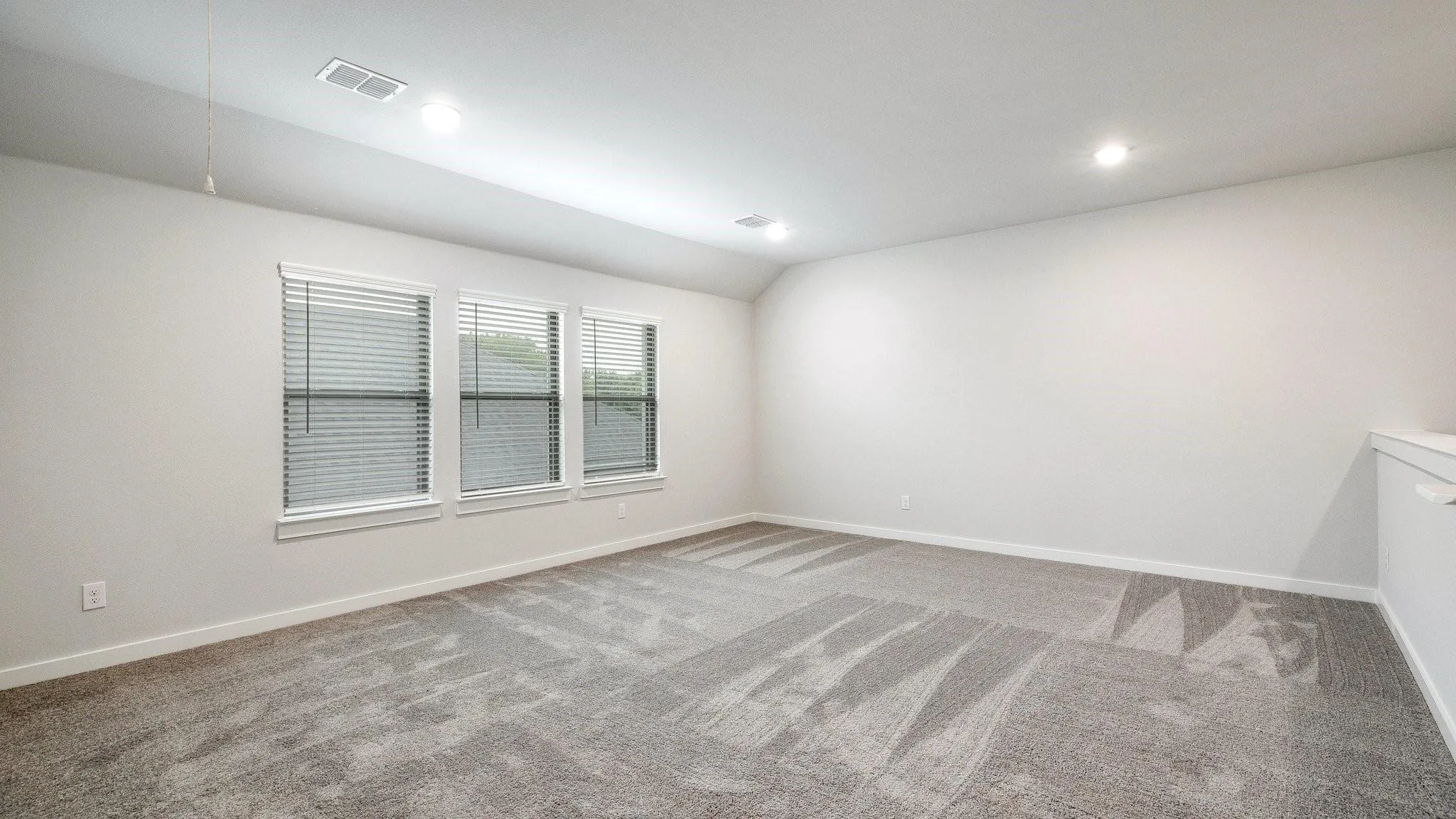Spacious room featuring neutral carpeting, a trio of windows with horizontal blinds, and recessed lighting