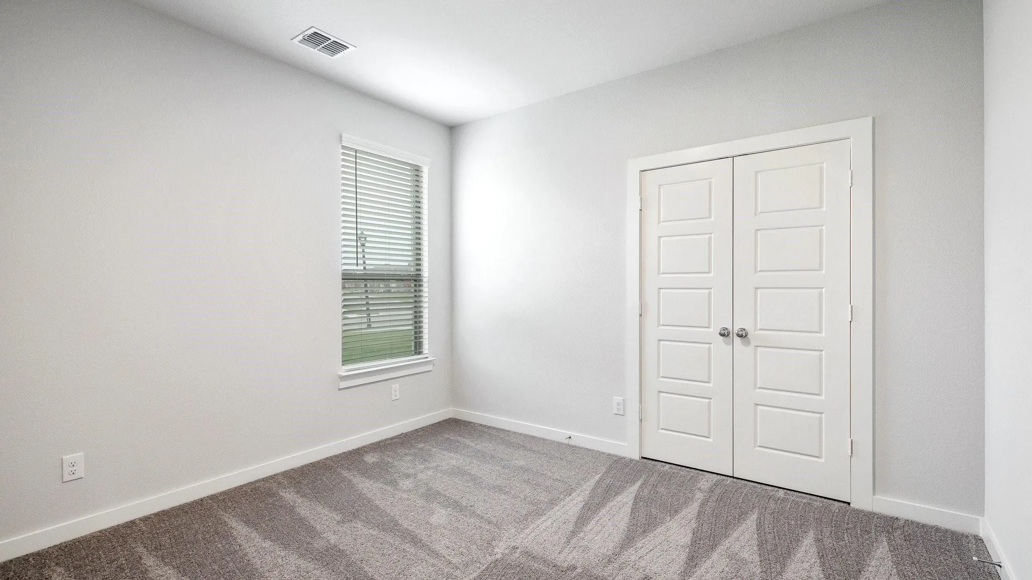 White paneled bifold doors, window with horizontal blinds, light gray wall finishes, and patterned carpet flooring
