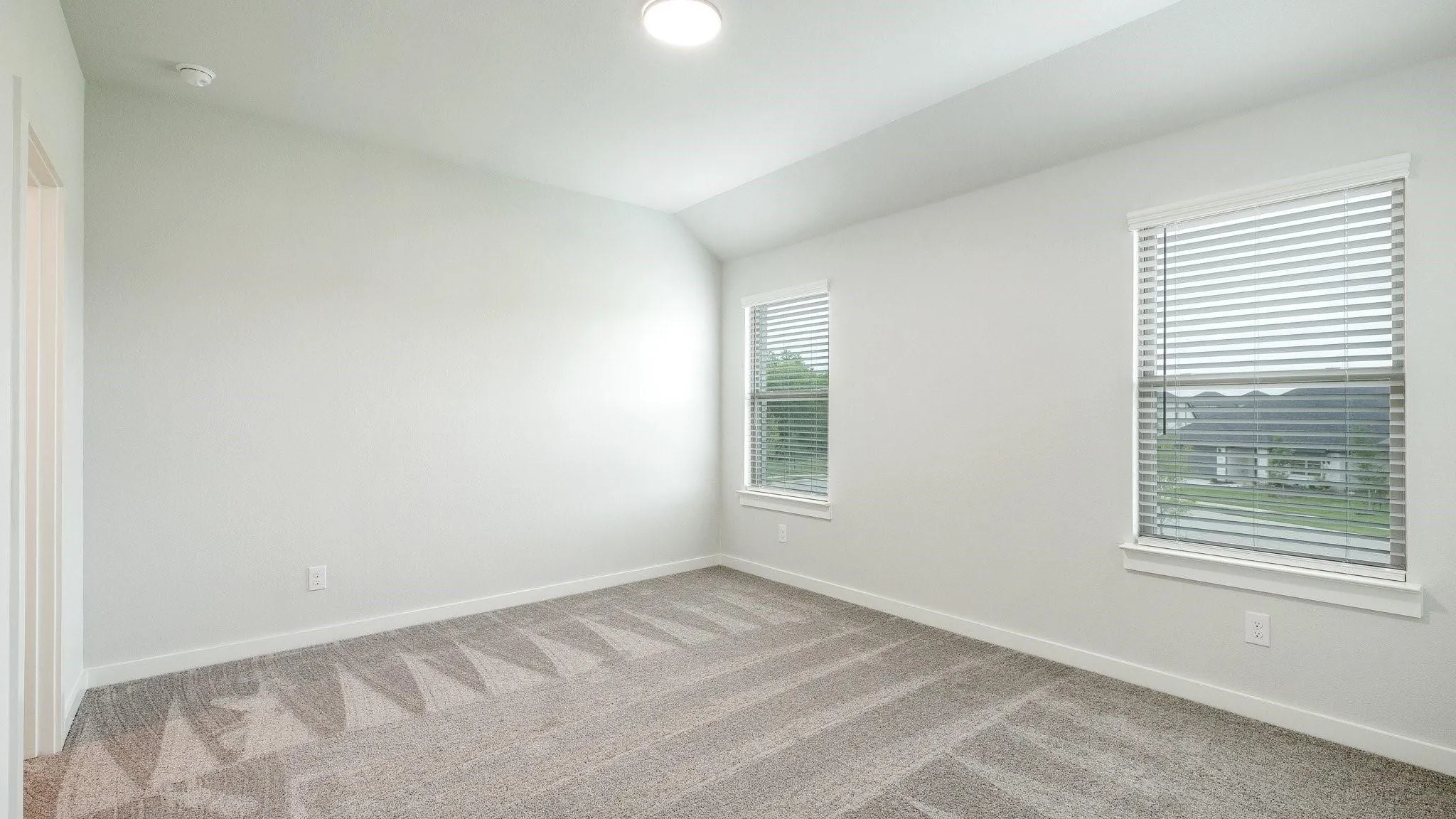 Recessed lighting, sloped ceiling, two windows with blinds, and patterned carpet flooring