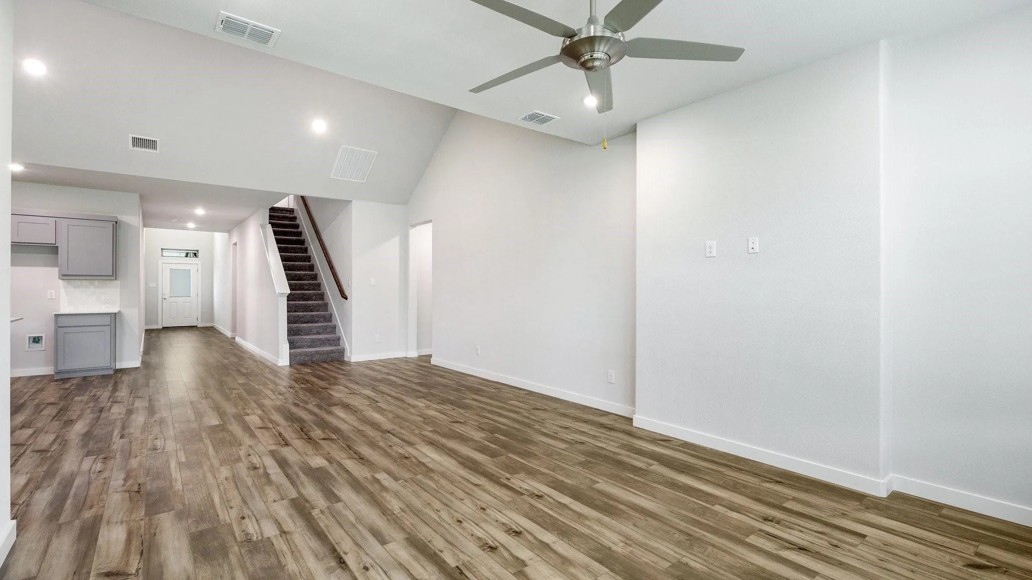 Vaulted ceiling with a ceiling fan, wood-finish flooring, recessed lighting, carpeted stairs with wood handrail, and gray cabinetry with white countertops