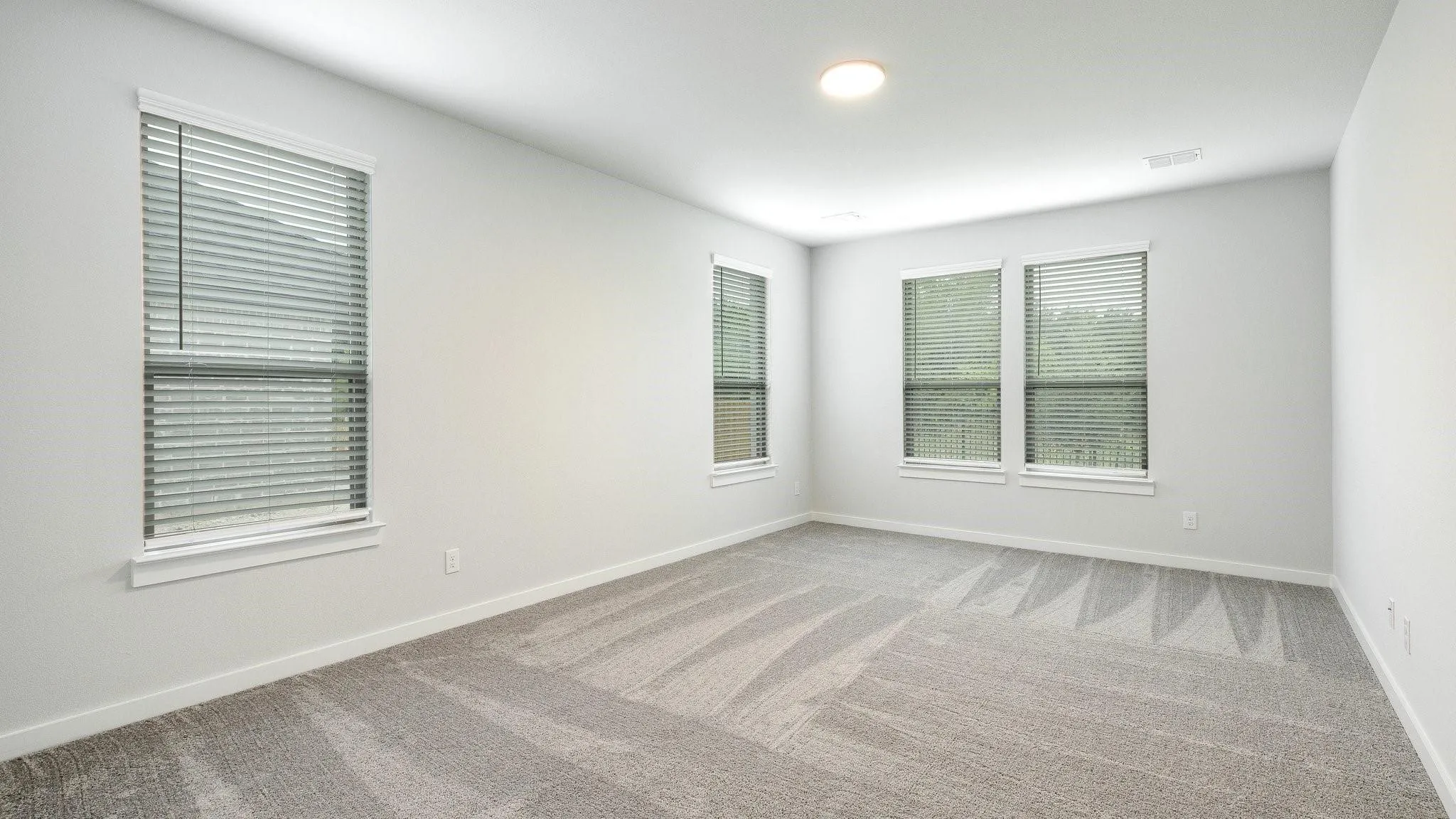 Bright corner bedroom with abundant natural light from multiple windows featuring horizontal blinds