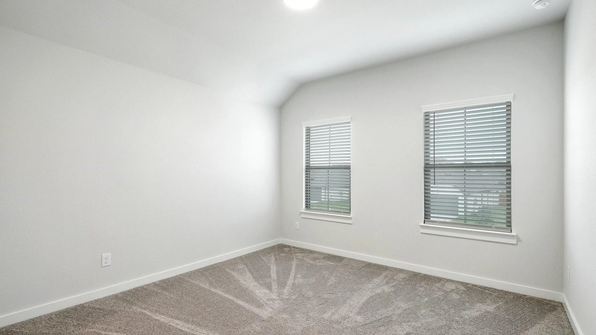Bright corner bedroom featuring dual windows with plantation shutters, neutral wall finishes, and plush carpeting throughout
