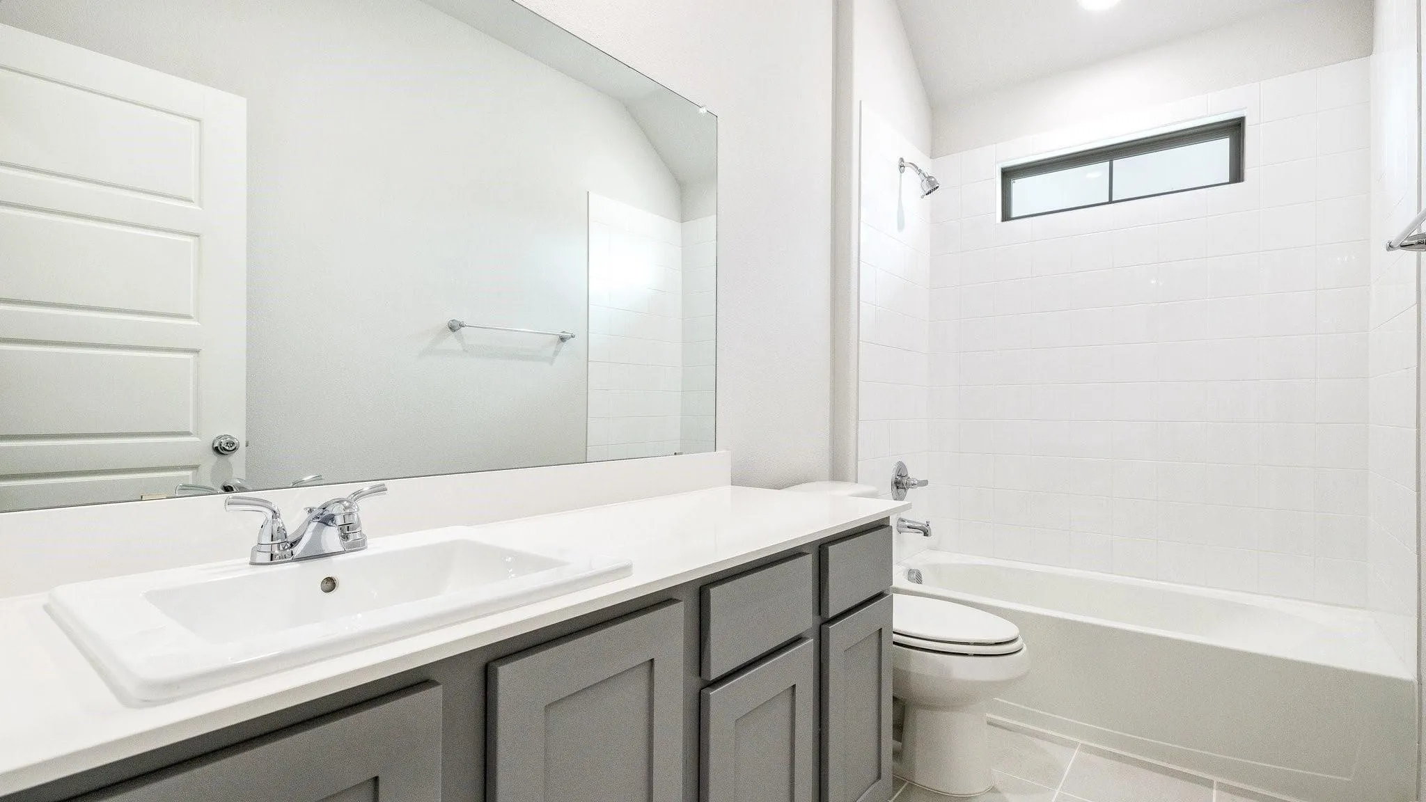Modern bathroom featuring a double-sink vanity with gray cabinetry, white quartz countertop, and polished chrome fixtures