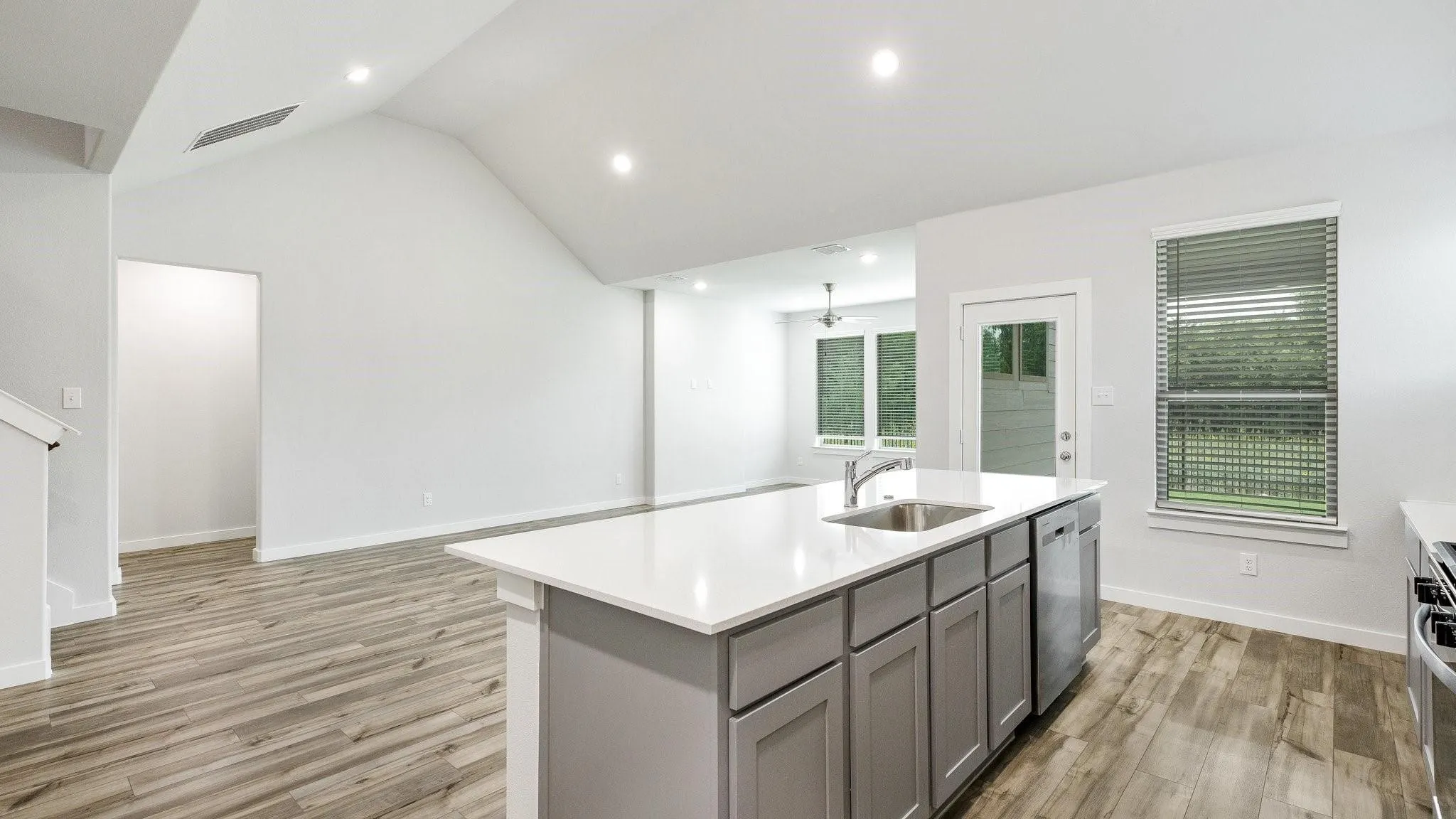 Modern kitchen featuring a large center island with gray cabinetry and white quartz countertop, stainless steel appliances, wood-finish flooring throughout, recessed lighting, and abundant natural light from multiple windows and glass doors