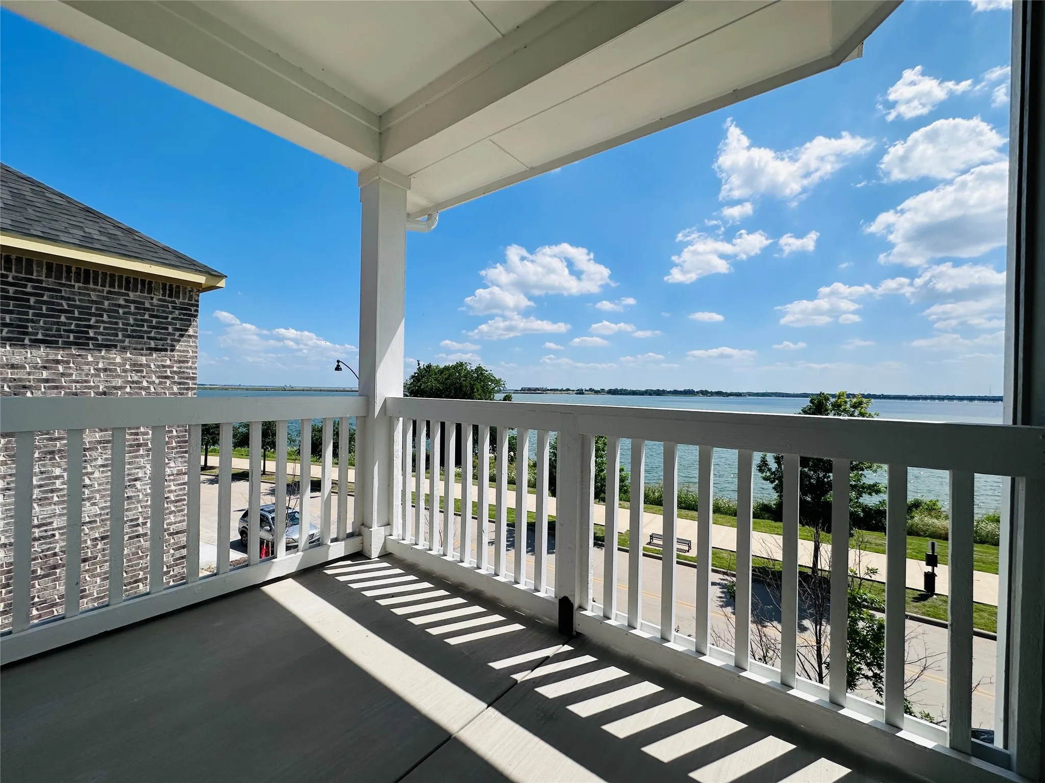 Spacious balcony with a water backdrop, featuring a white railing, exposed aggregate flooring, and a columned overhang