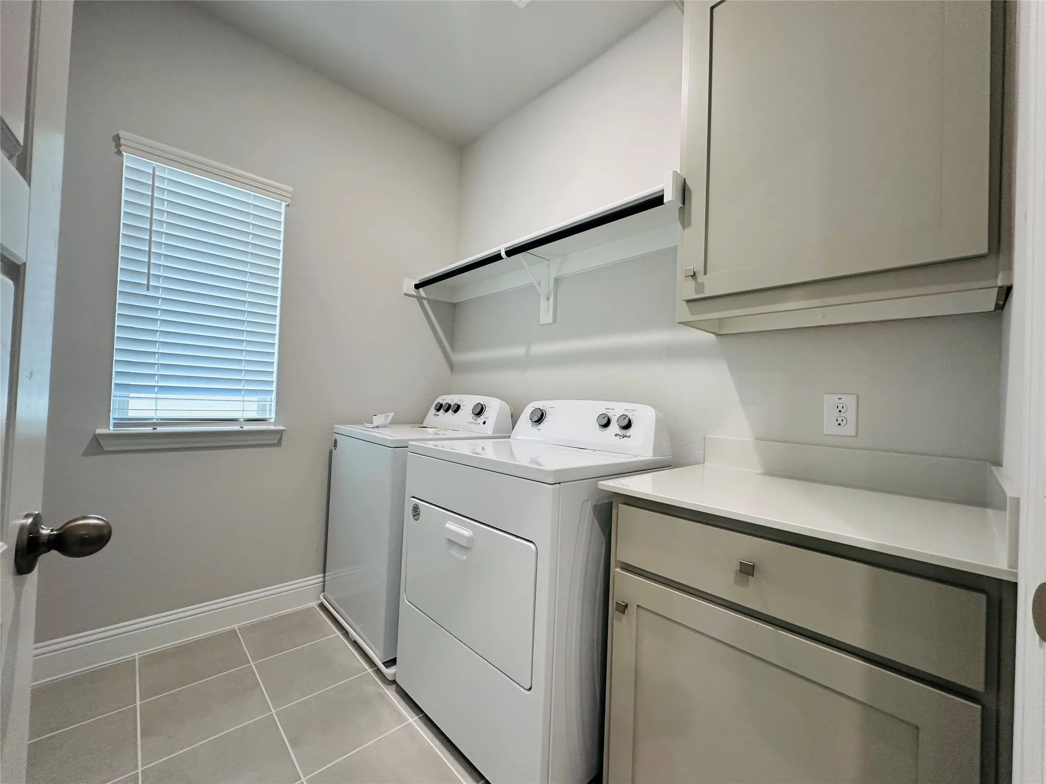 Laundry room with tile flooring, built-in shelving, window with blinds, upper cabinetry, and lower cabinetry with a countertop