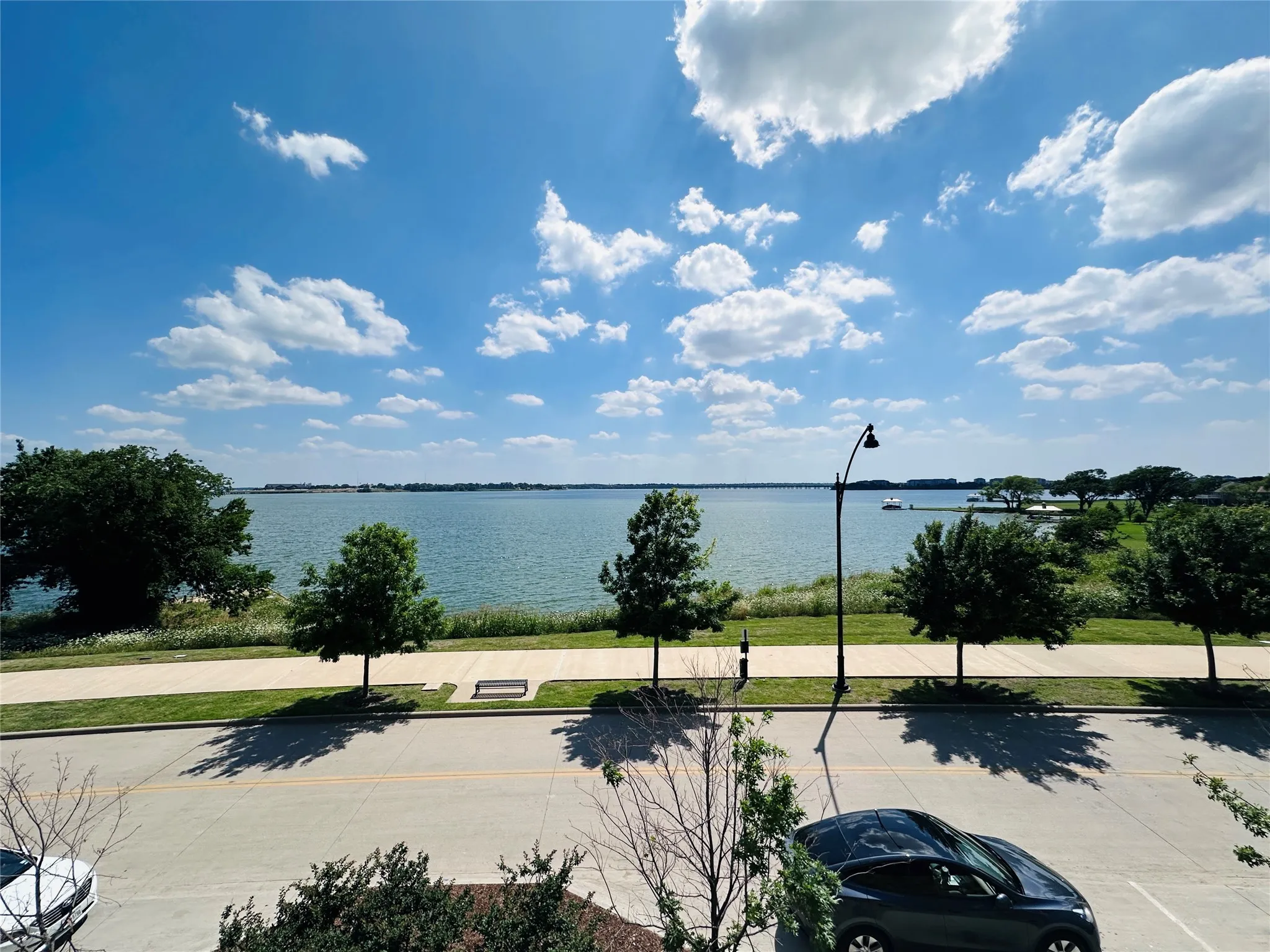 Expansive lakefront setting with a paved walking path, mature trees, and a clear blue sky