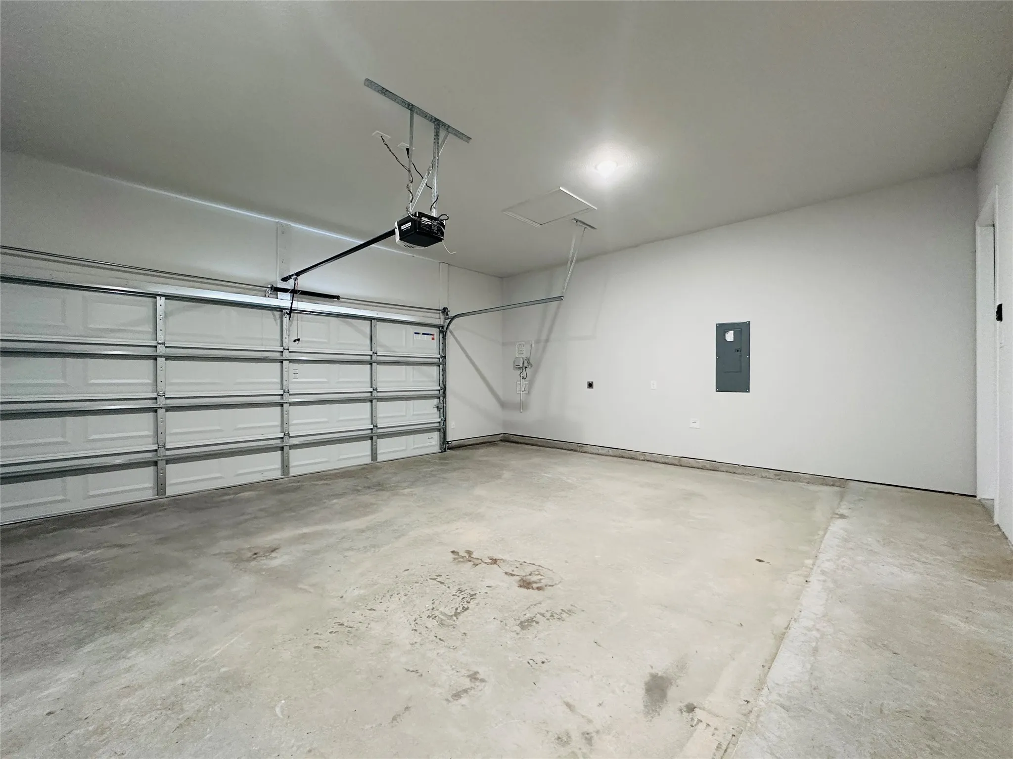 Attached garage with a sectional door, automatic opener, concrete flooring, and ceiling-mounted lighting