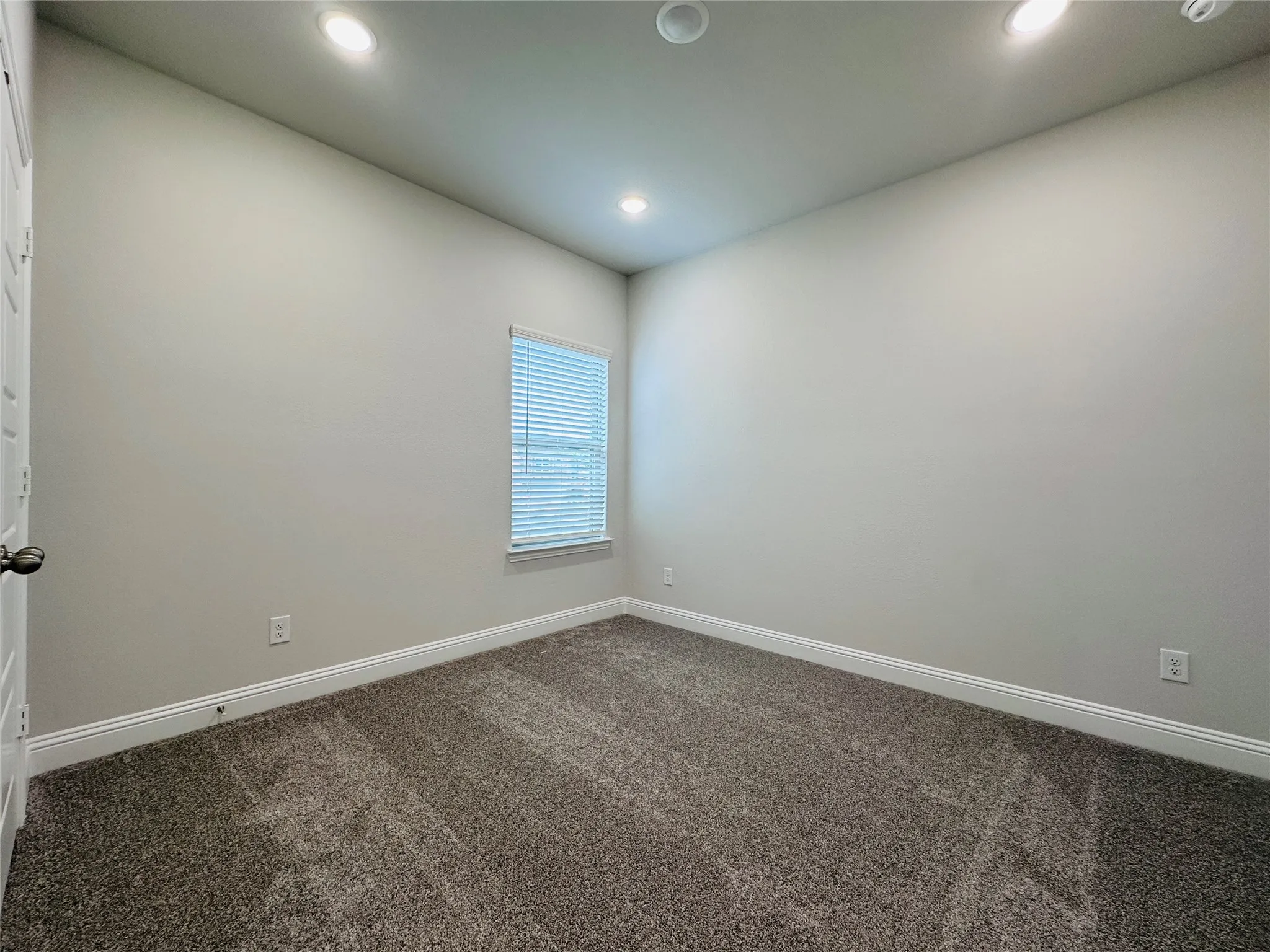 Bright and spacious bedroom featuring recessed ceiling lighting, neutral wall finishes, carpet flooring, and a window with plantation shutters allowing natural light throughout the room