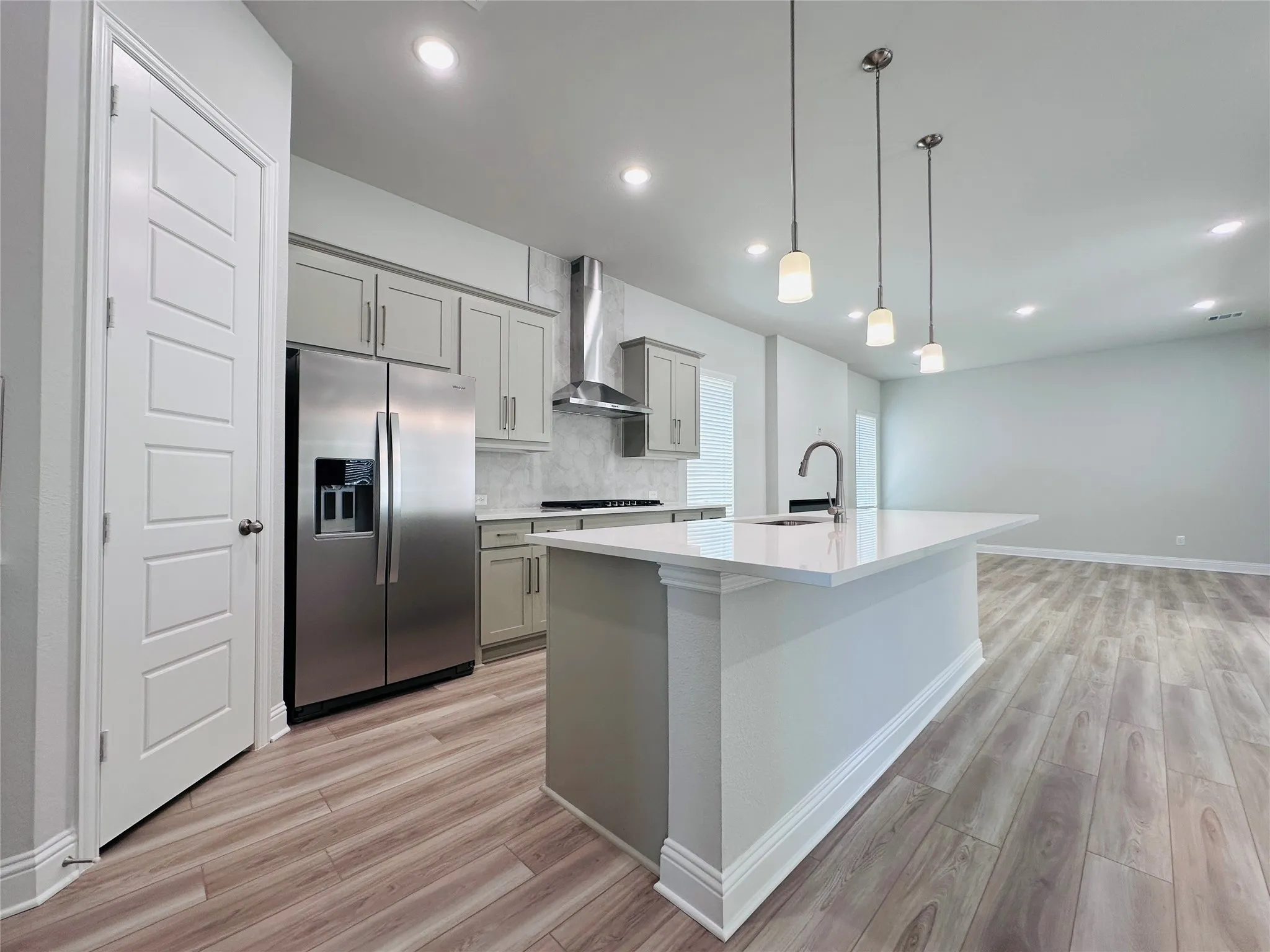 Open-concept kitchen with light wood-finish flooring, a central island featuring a gooseneck faucet, light-toned cabinetry, stainless steel appliances, and recessed lighting