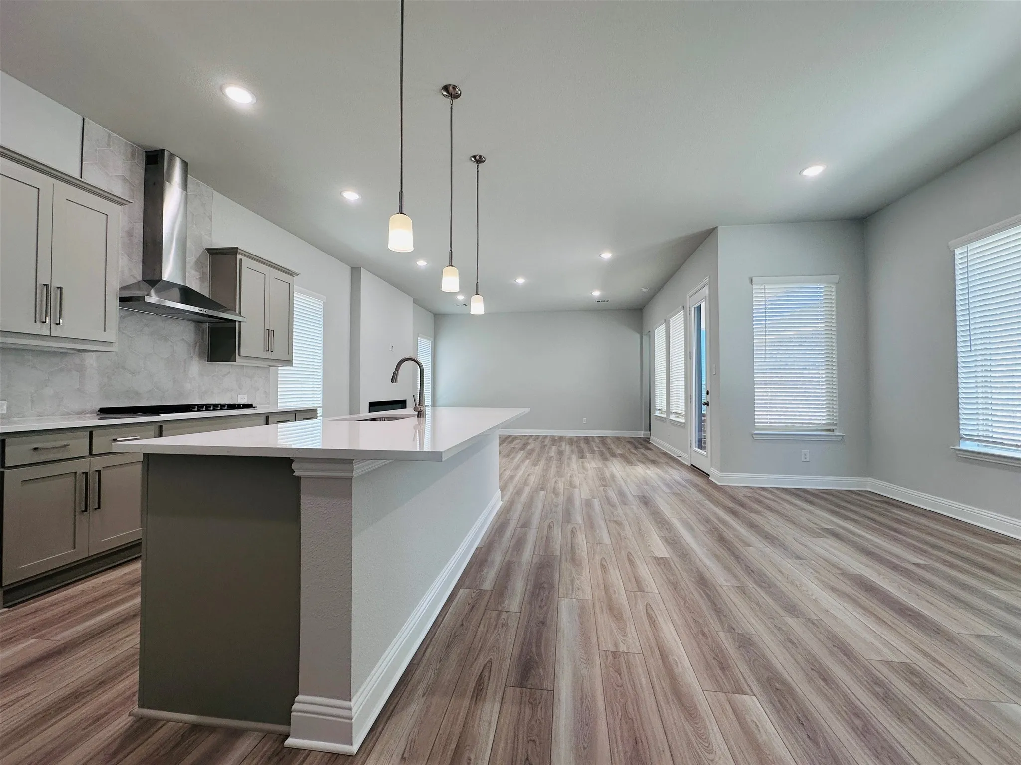 Kitchen island with a white countertop, recessed lighting, wood-finish flooring, a stainless steel range hood, and multiple windows
