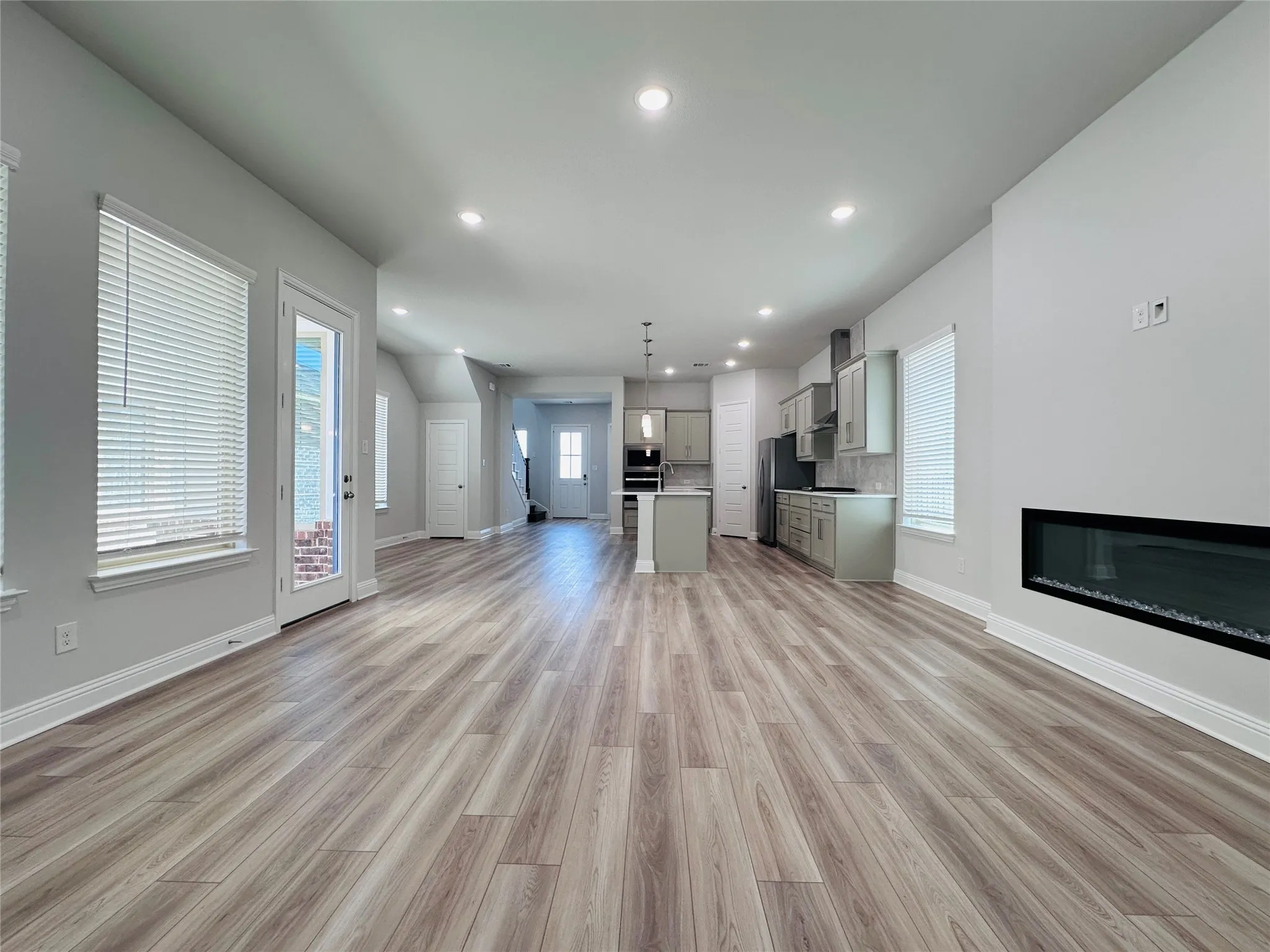 Open-concept living space with wood-finish flooring, recessed lighting, and a linear electric fireplace
