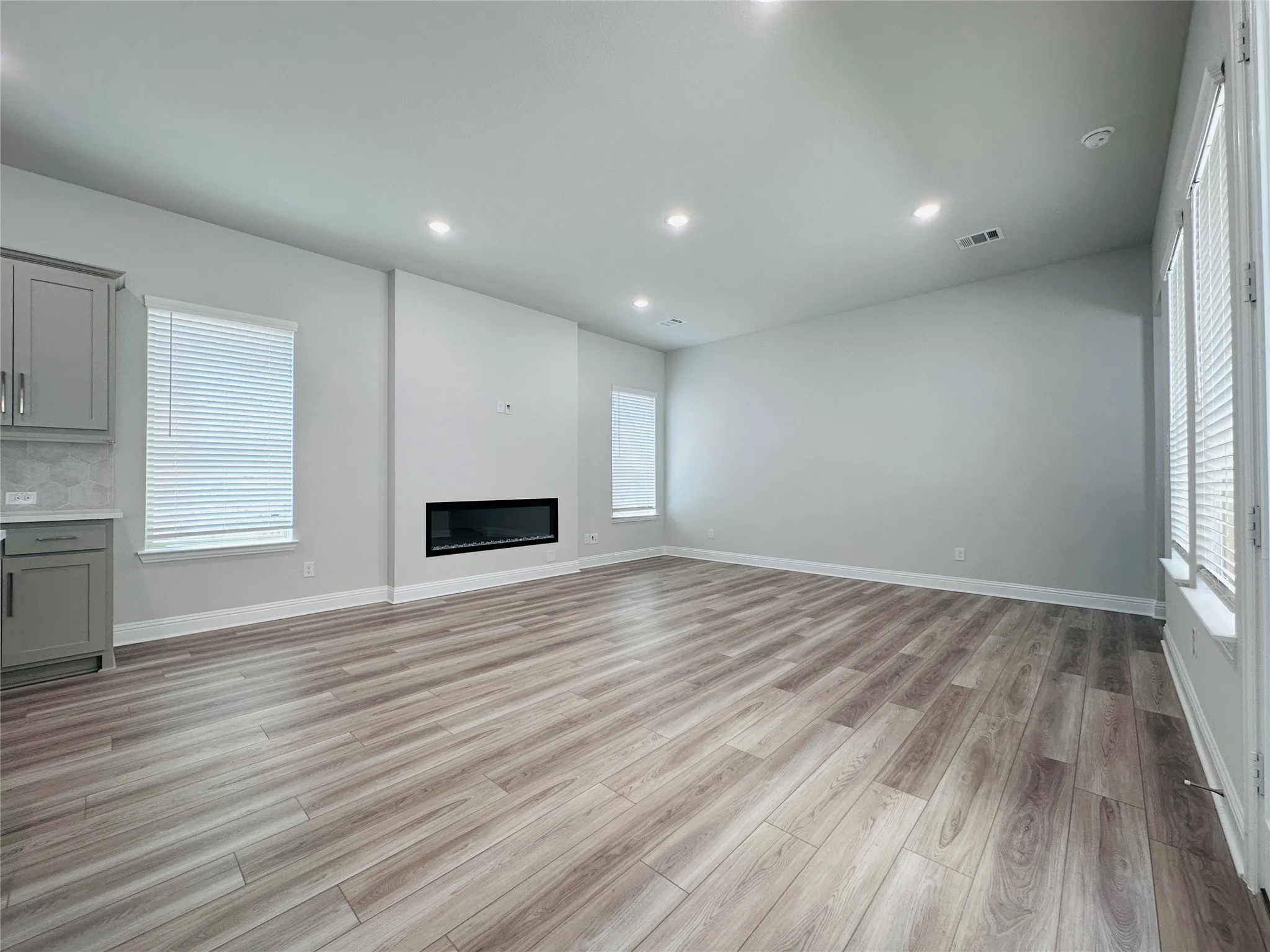 Spacious living area featuring wood-finish flooring, a modern linear fireplace, recessed lighting, and ample natural light from multiple windows