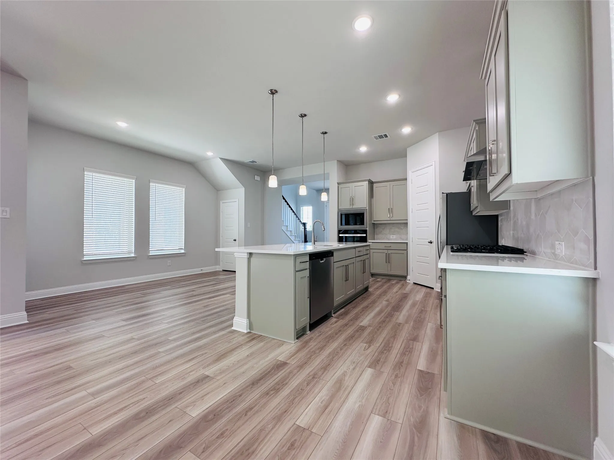 Wood-finish flooring throughout, kitchen with light-toned cabinetry and white countertops, recessed ceiling lighting, and stainless steel appliances