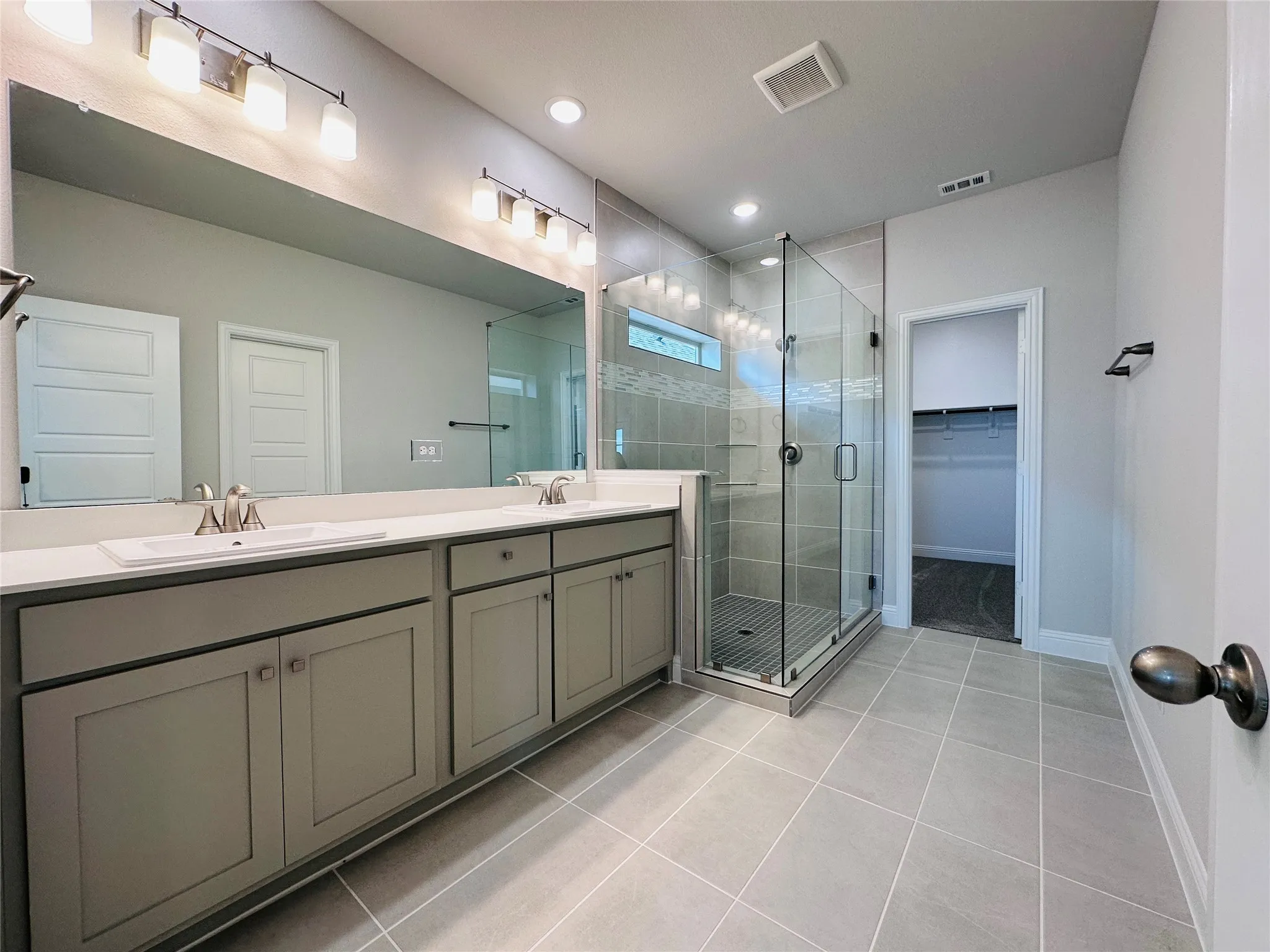 Dual vanity with under-sink cabinetry, extensive vanity mirror, glass-enclosed shower, tiled flooring, and recessed lighting