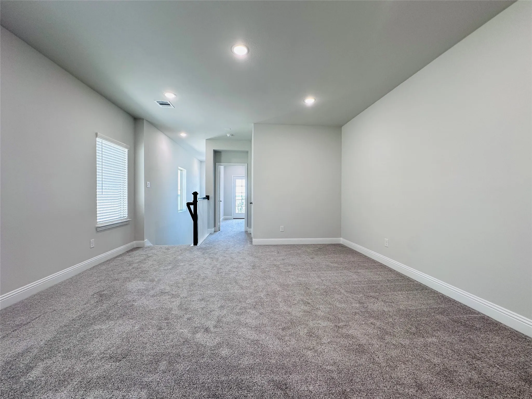 Spacious carpeted area with recessed lighting, white baseboards, and window with blinds