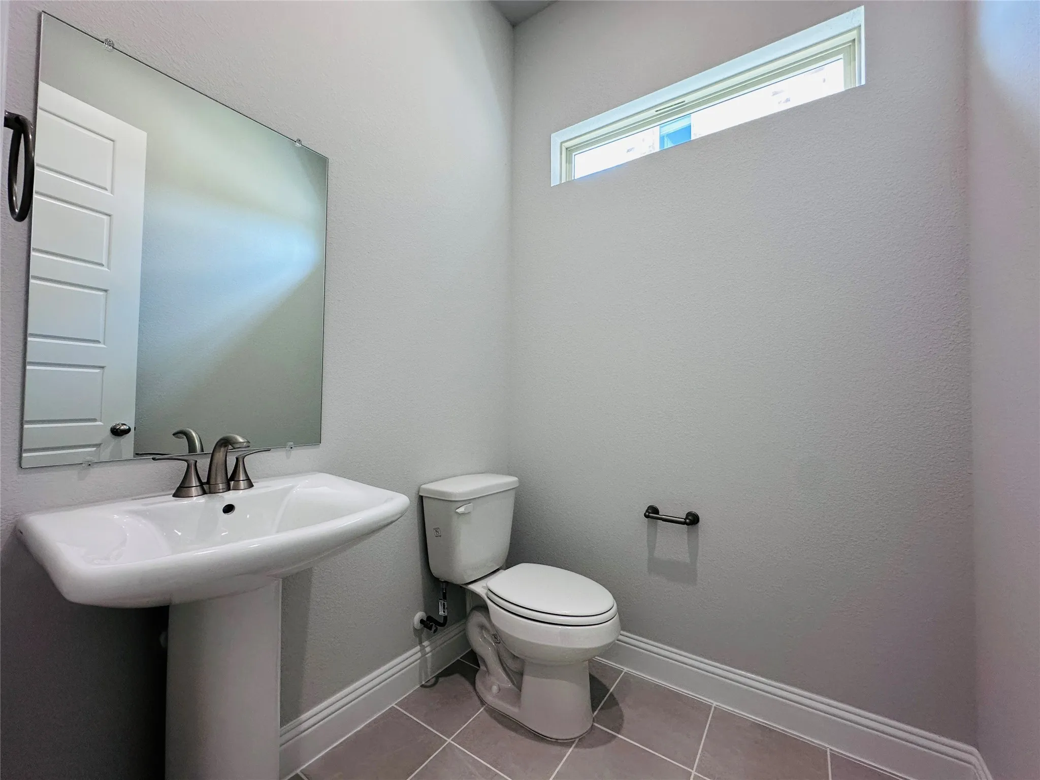 Pedestal sink with brushed nickel faucet, wall-mounted mirror, transom window, and tiled flooring