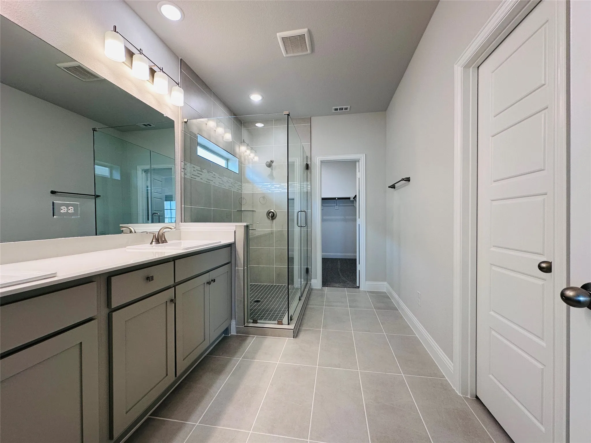 Dual vanity with stone countertop, walk-in shower with glass enclosure, tiled flooring, and paneled interior door