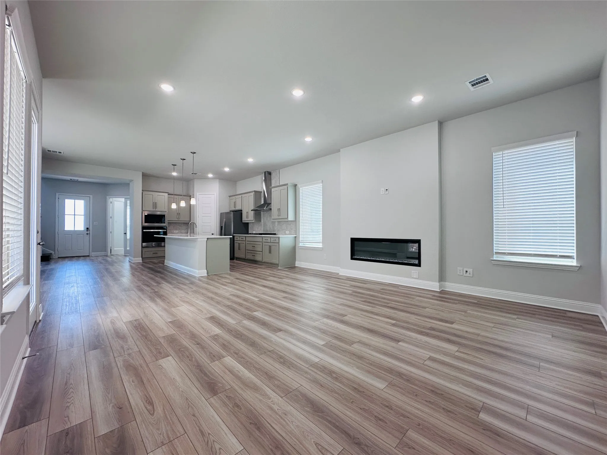 Open-concept living area featuring wood-finish flooring, recessed lighting, and a linear electric fireplace