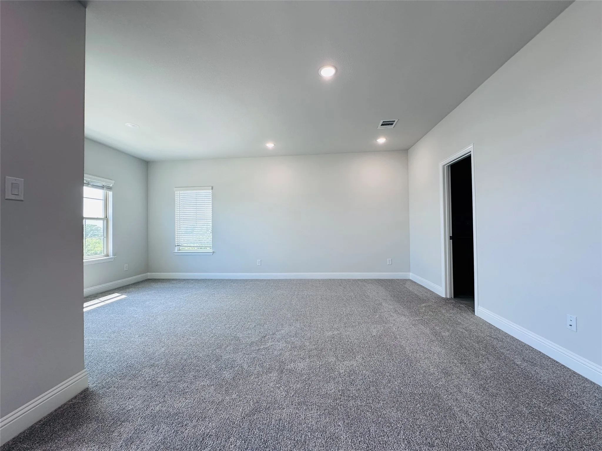 Spacious open room featuring neutral wall finishes, recessed ceiling lighting, carpeted flooring, and abundant natural light from dual windows