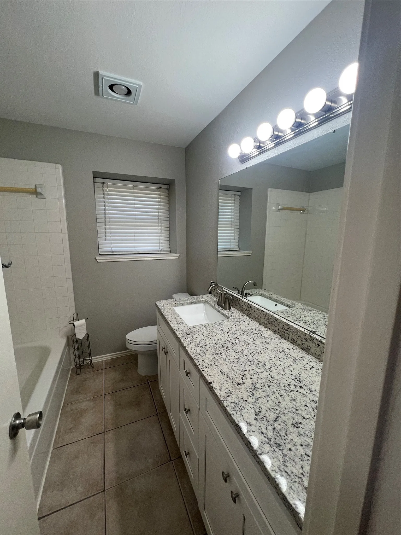 White vanity with brushed nickel hardware, ample countertop space, and large mirror with overhead lighting