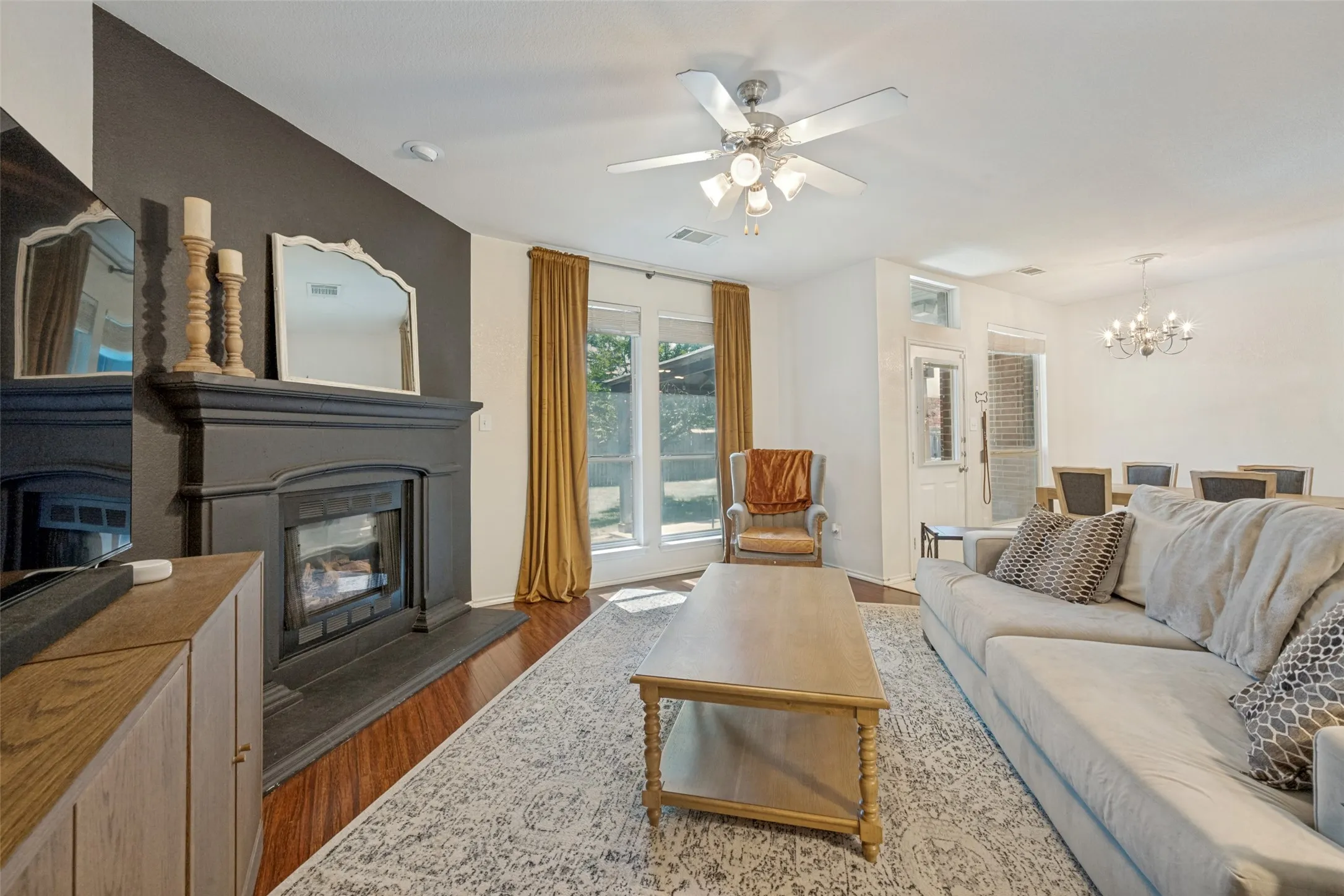 Spacious living room featuring a wood-burning fireplace with custom cabinetry, ceiling fan with integrated lighting, wood-finish flooring throughout, and glass sliding doors opening to outdoor space