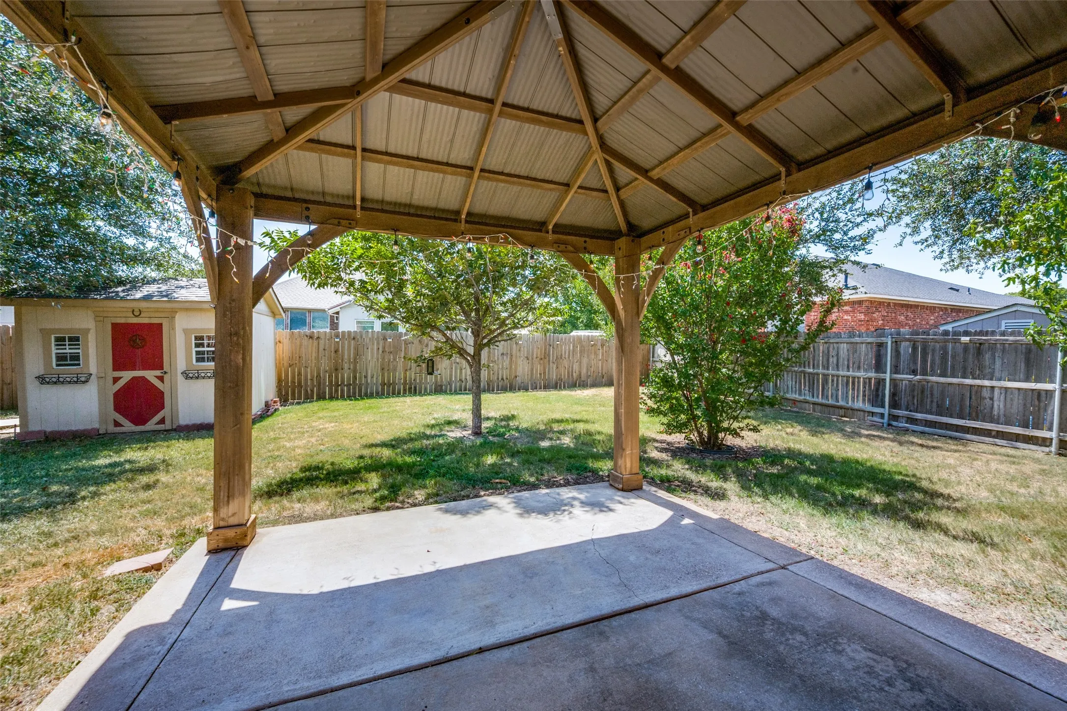 Covered patio with a concrete slab, backyard lawn, wood privacy fencing, and a separate storage shed
