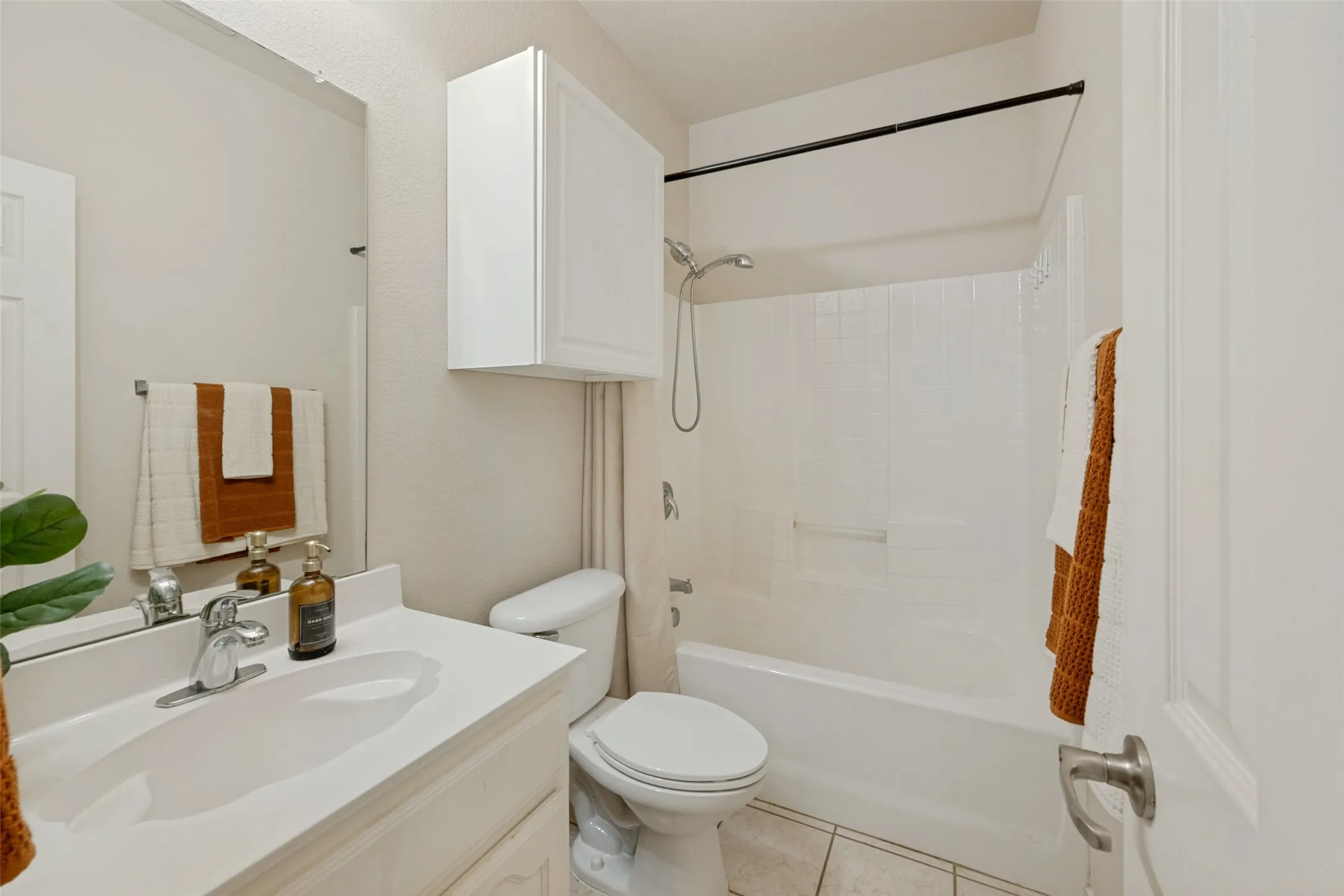 Clean, bright bathroom featuring a white vanity with integrated sink and faucet, mirrored medicine cabinet with overhead lighting, ceramic tile flooring, white subway tile shower surround with chrome fixtures, and a toilet with chrome hardware