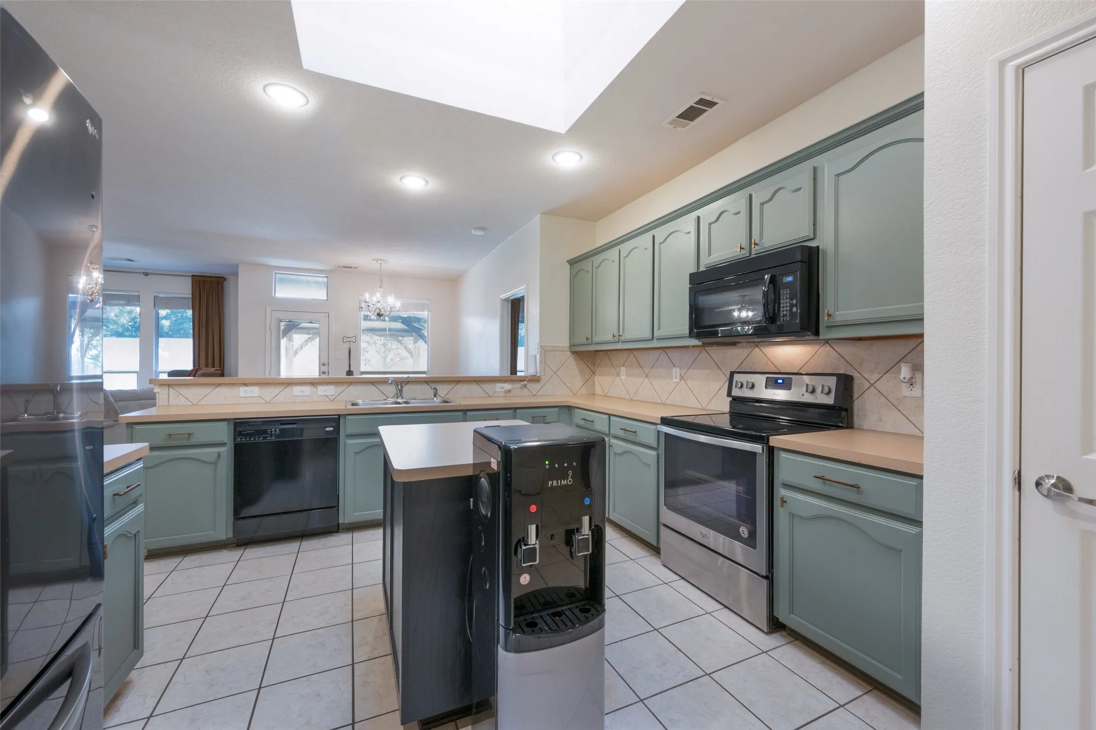 Spacious kitchen featuring green cabinetry, a tile backsplash, stainless steel appliances, and tile flooring