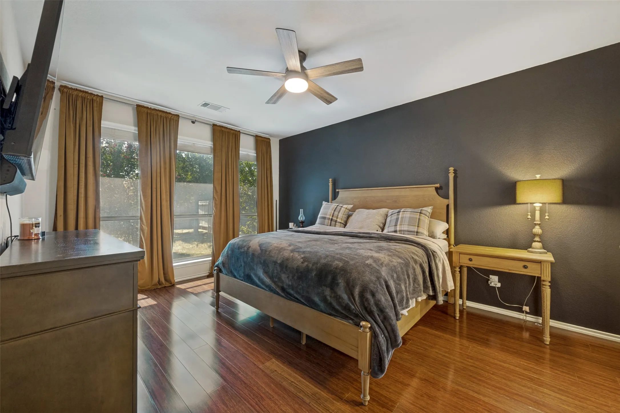 Wood-finish flooring, accent wall, ceiling fan, and multiple windows