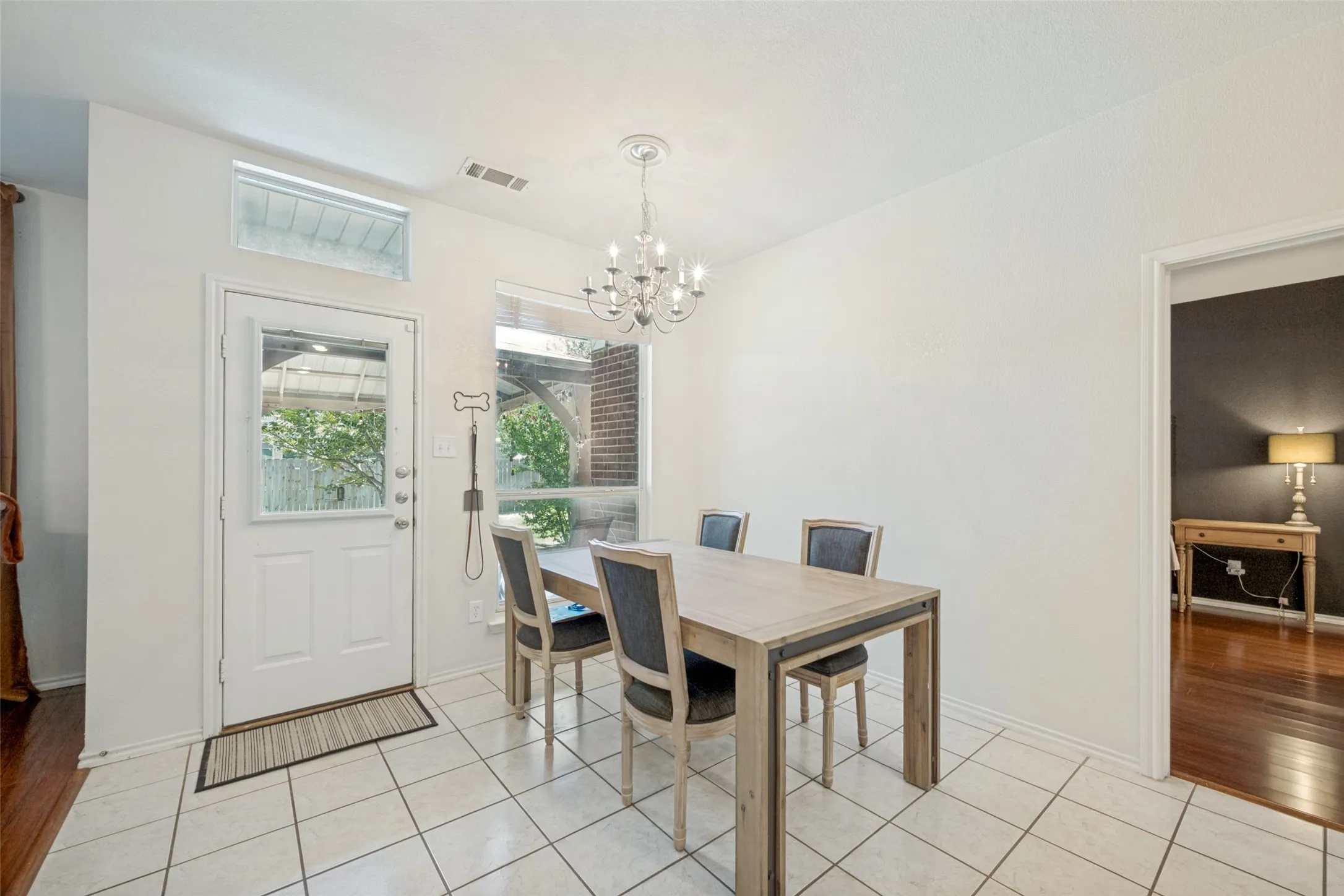 Tiled flooring, transom window, chandelier, and a white paneled door with glass insert