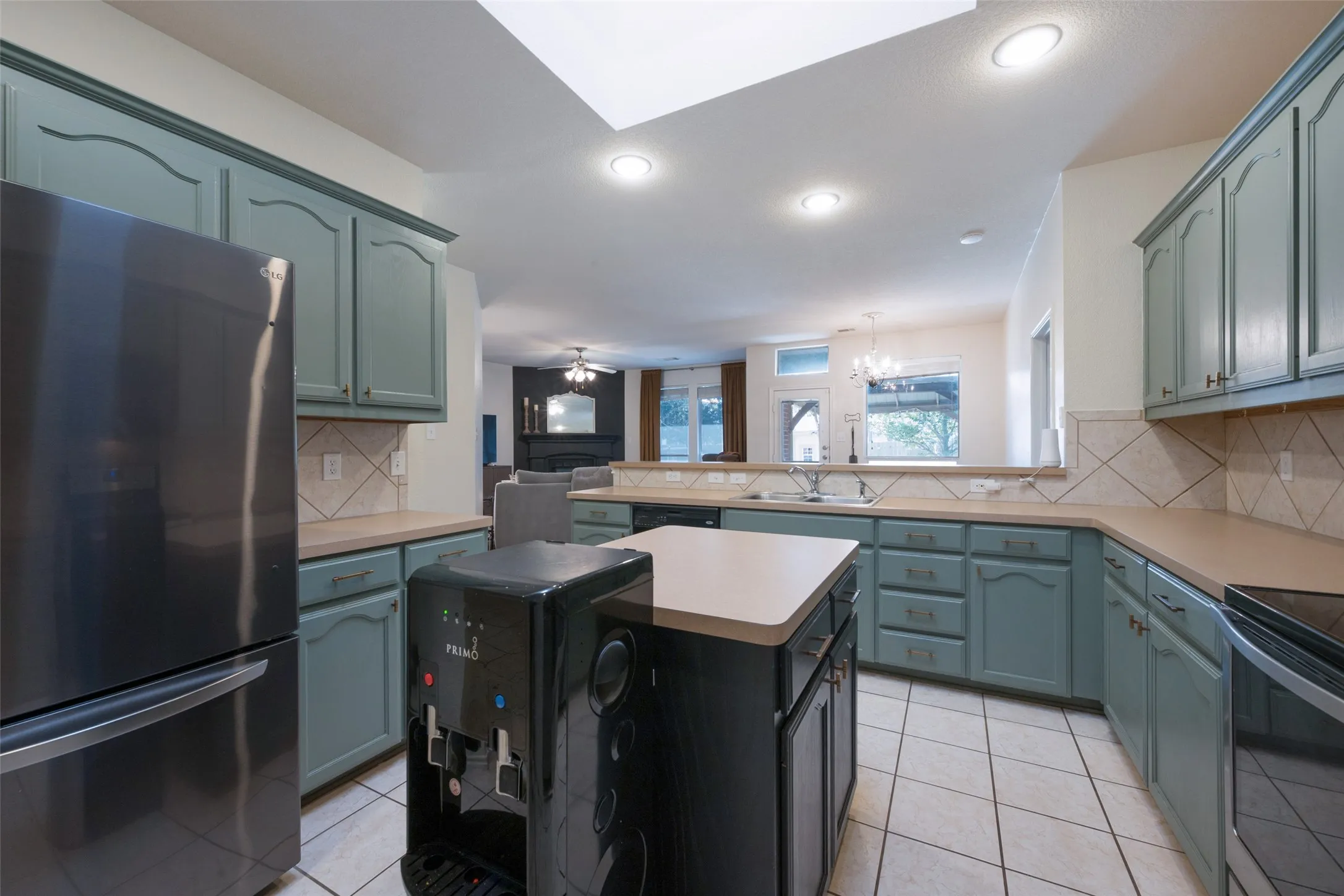 Kitchen featuring green cabinetry, a center island with a light-toned countertop, a tile backsplash, and recessed lighting and a generous sky light