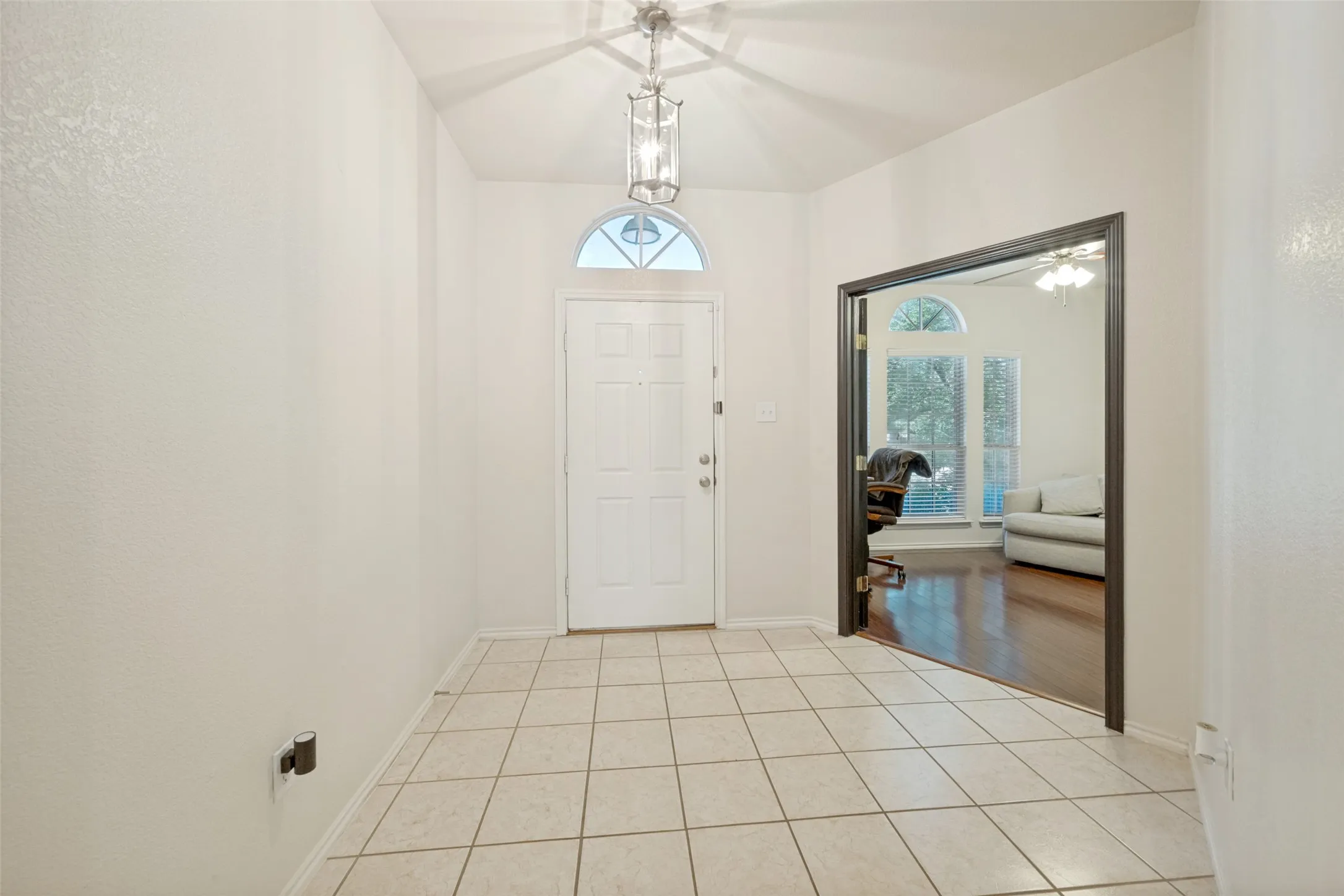 Vaulted entry ceiling, tile flooring, recessed arched transom window, and a chandelier-style light fixture