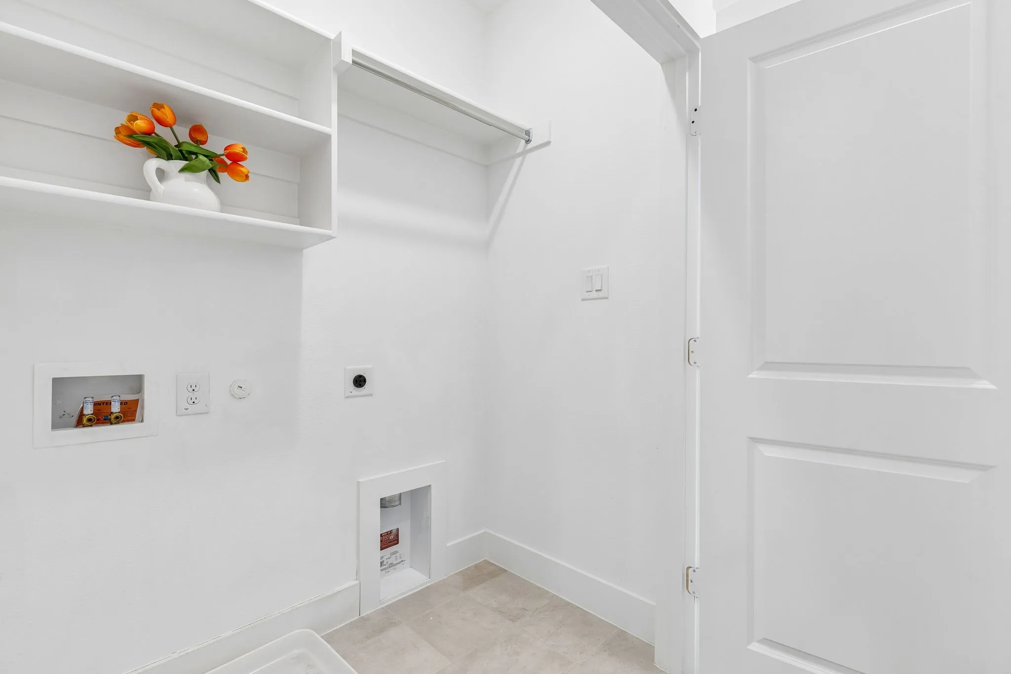 Laundry area with built-in shelving, clothing rod, and neutral tile flooring