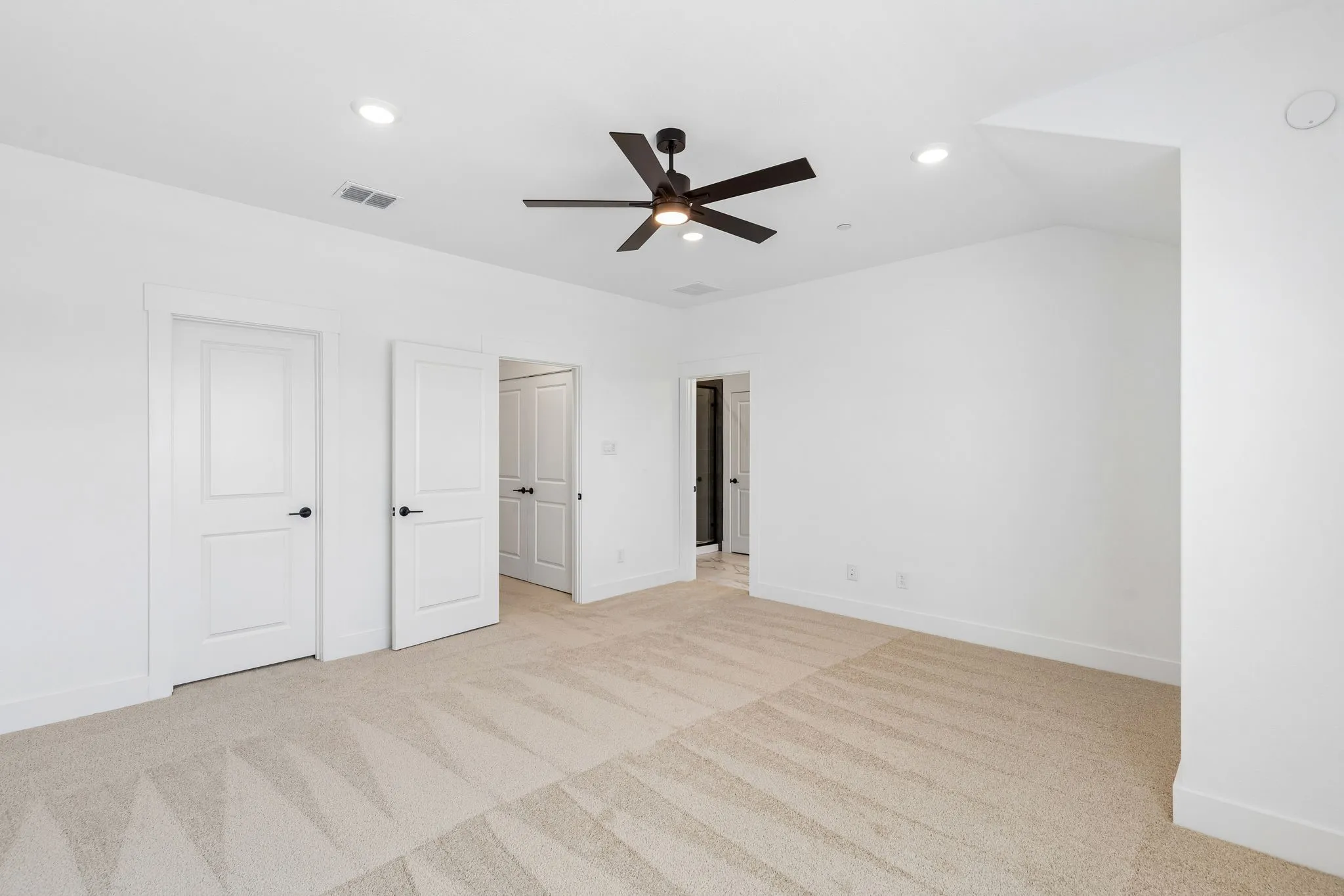 Spacious room featuring neutral carpeting, white walls, recessed lighting, and a ceiling fan