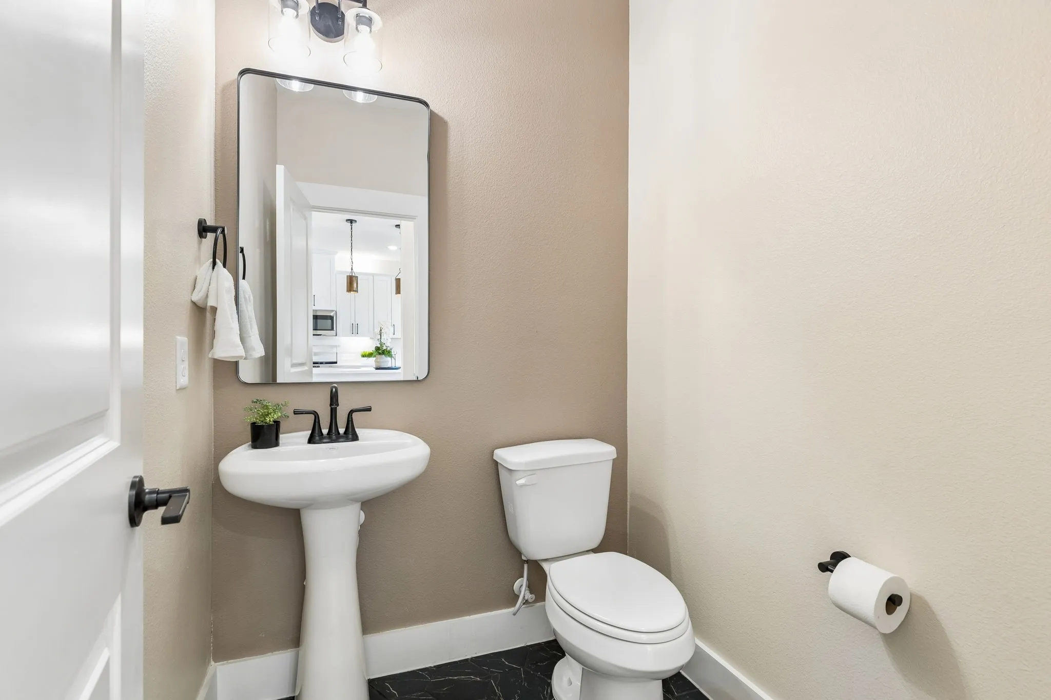 Pedestal sink with a matte black faucet, rectangular framed mirror, and contemporary vanity light fixture