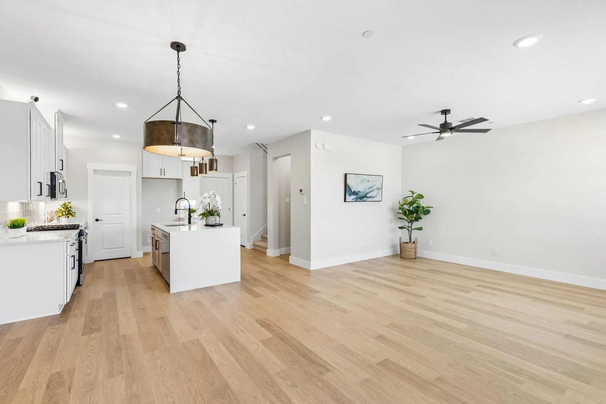 Open concept living area featuring light wood-finish flooring, recessed lighting, a modern ceiling fan, and a kitchen with white cabinetry and a central island