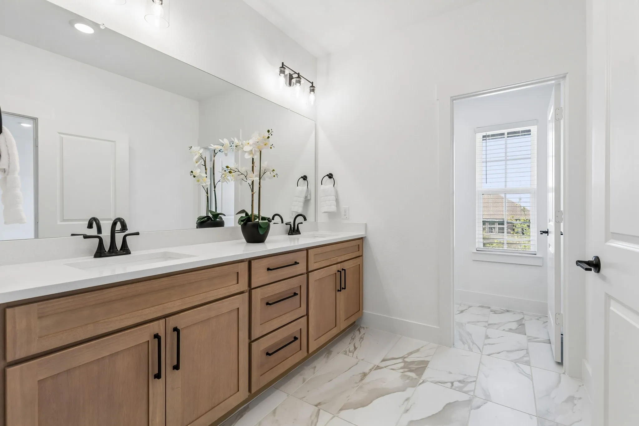 Double vanity with wood-finish cabinetry, white countertop, and matte black fixtures