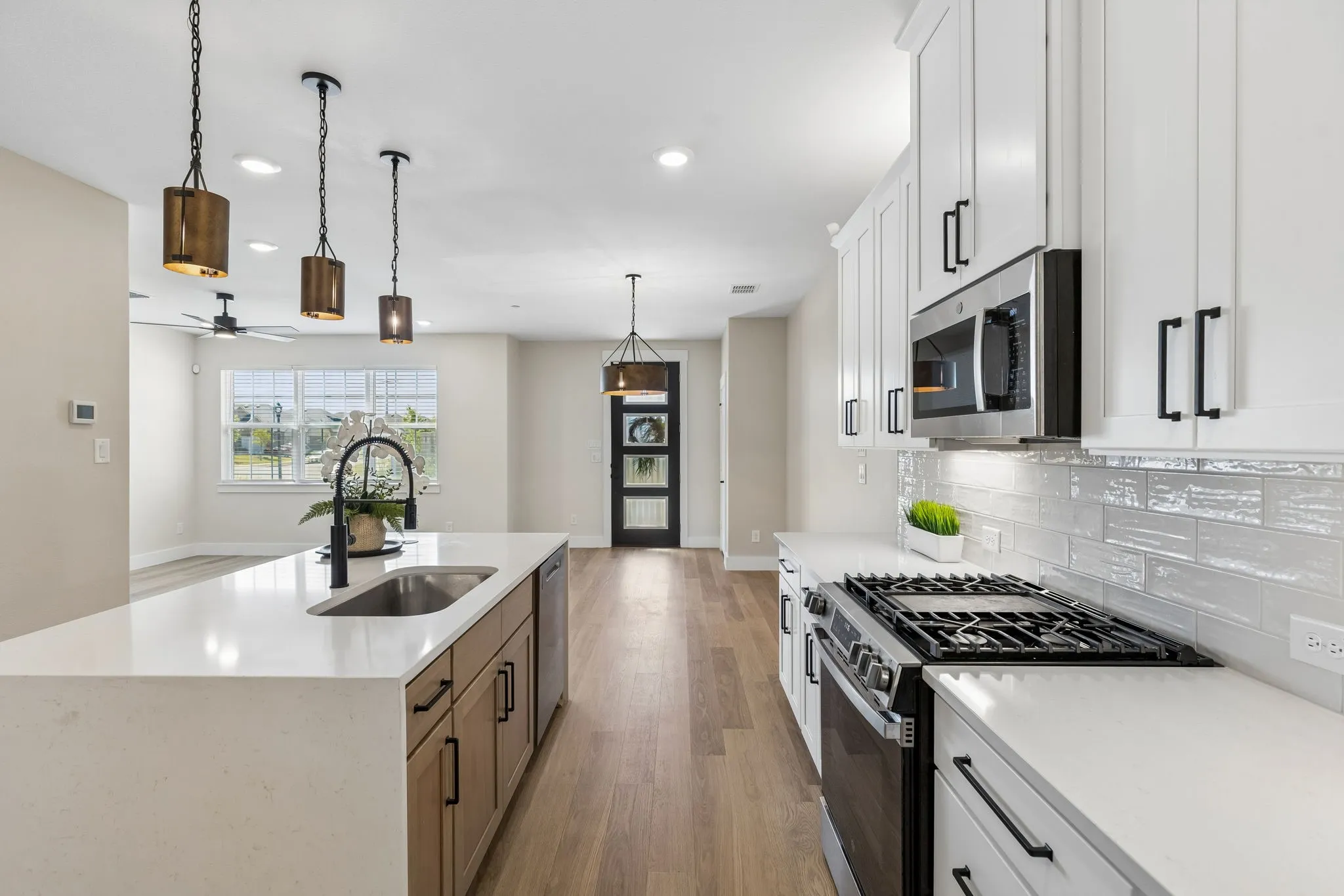 Spacious kitchen featuring an island with a built-in sink, stainless steel appliances, white cabinetry, light wood-finish flooring, and pendant lighting fixtures