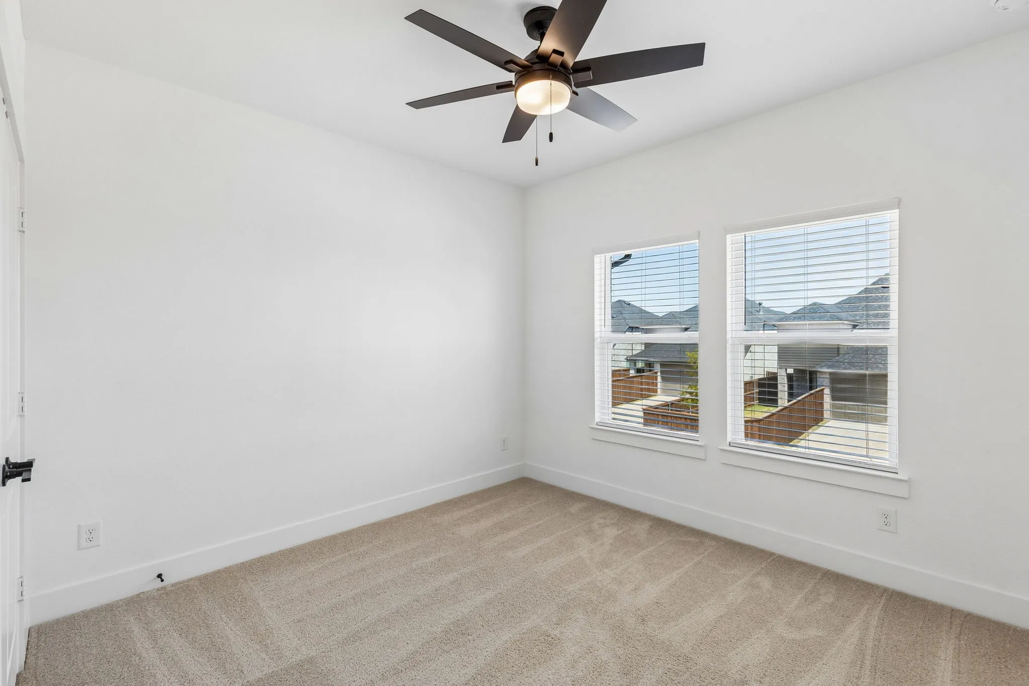 Neutral carpet flooring, dual pane windows with blinds, matte black ceiling fan with integrated lighting, white walls, and white trim