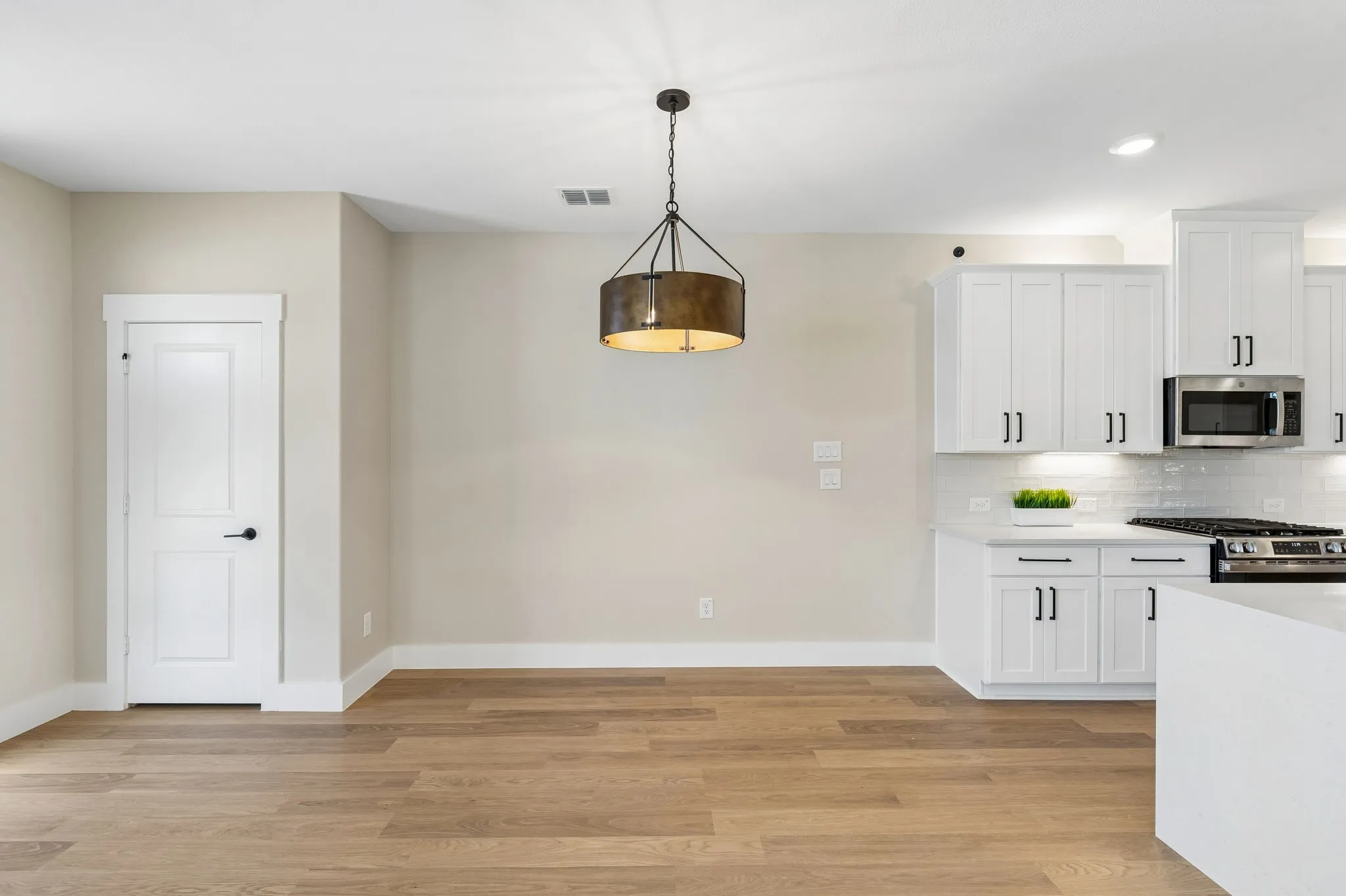 Wood-finish flooring, white paneled door, kitchen featuring white cabinetry, subway tile backsplash, and stainless steel appliances