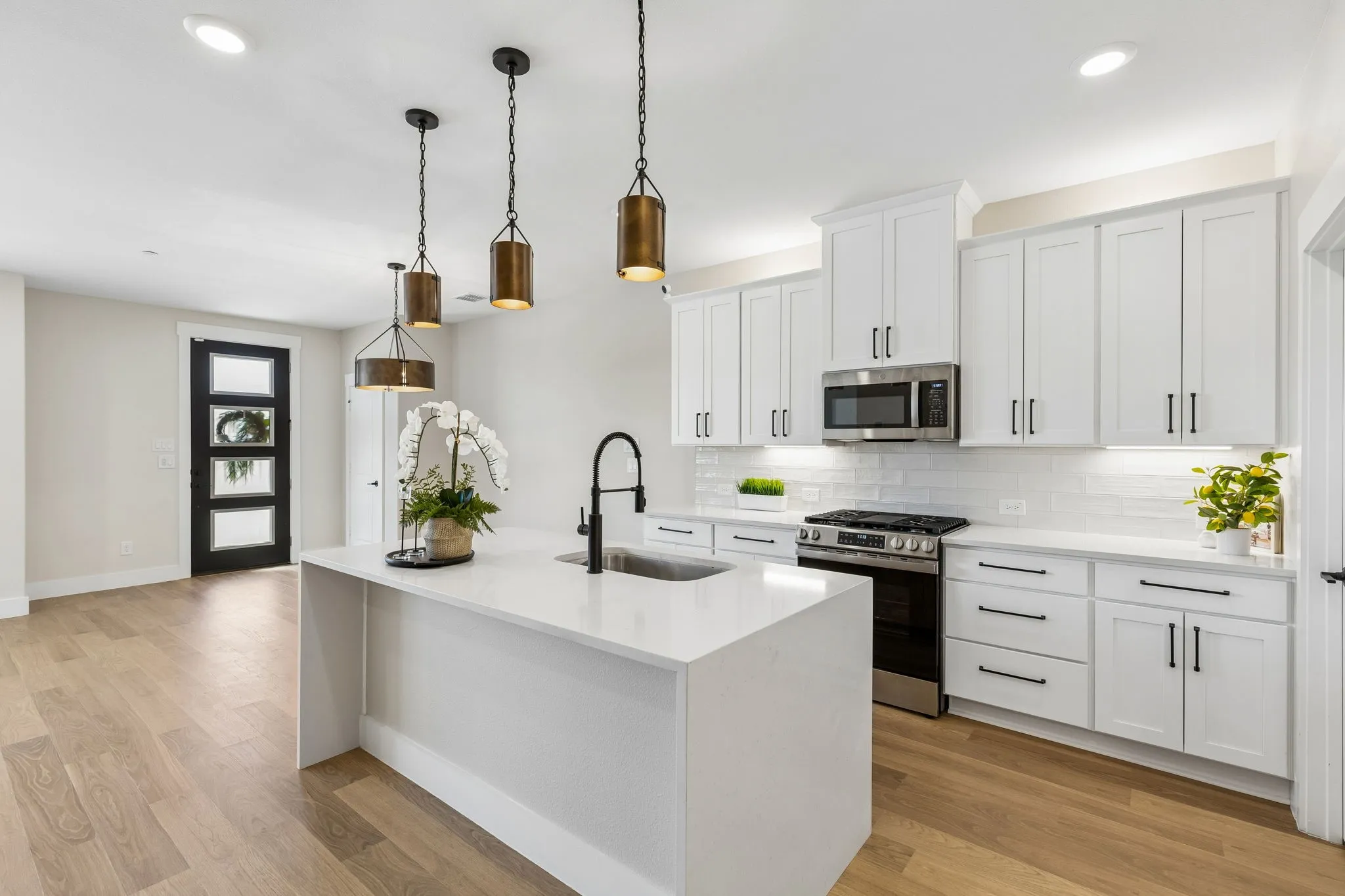 Modern kitchen featuring a waterfall island, white cabinetry, stainless steel appliances, and wood-finish flooring