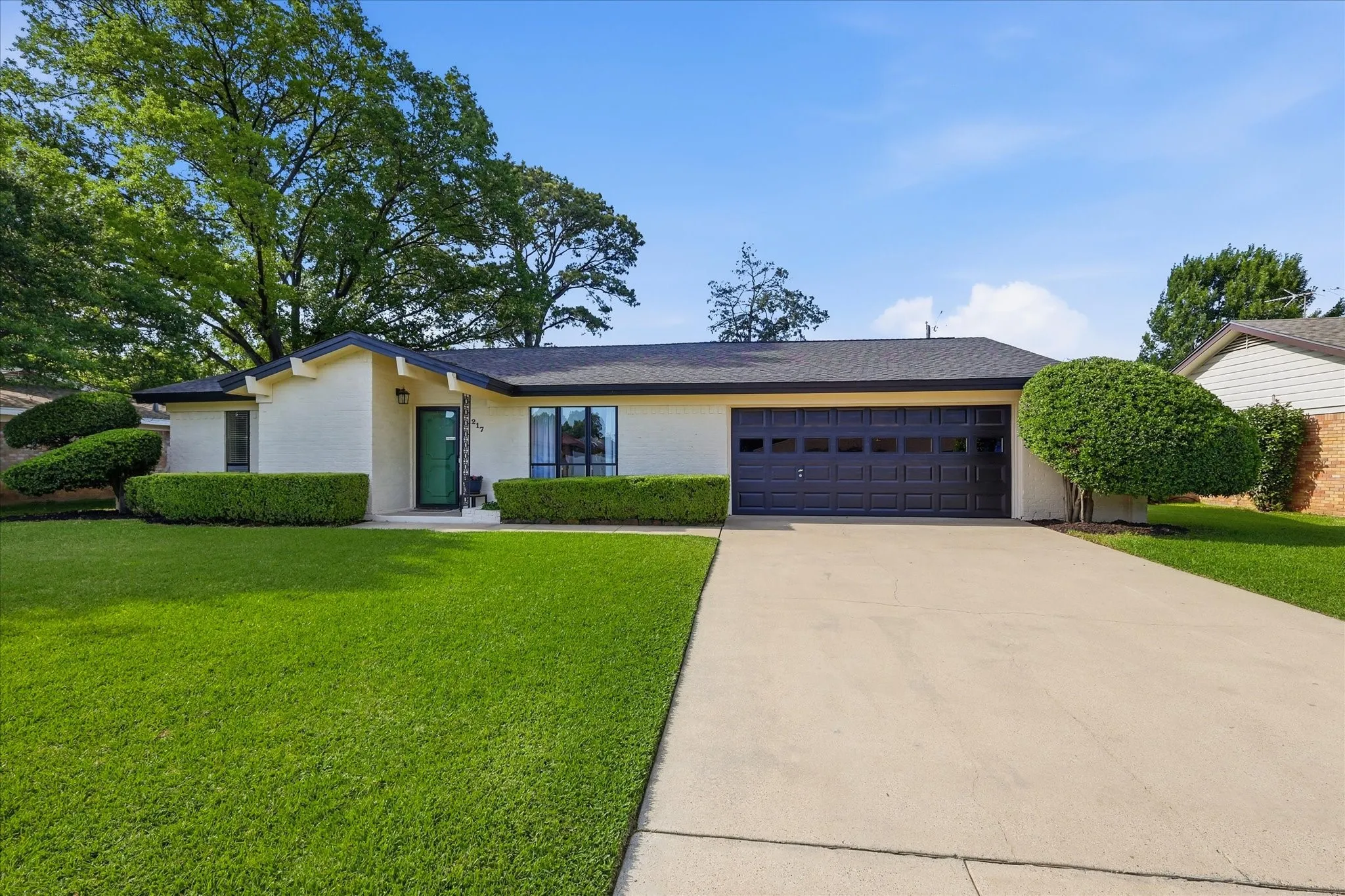 Single-story residence featuring a two-car garage, concrete driveway, and expansive front lawn with manicured hedges