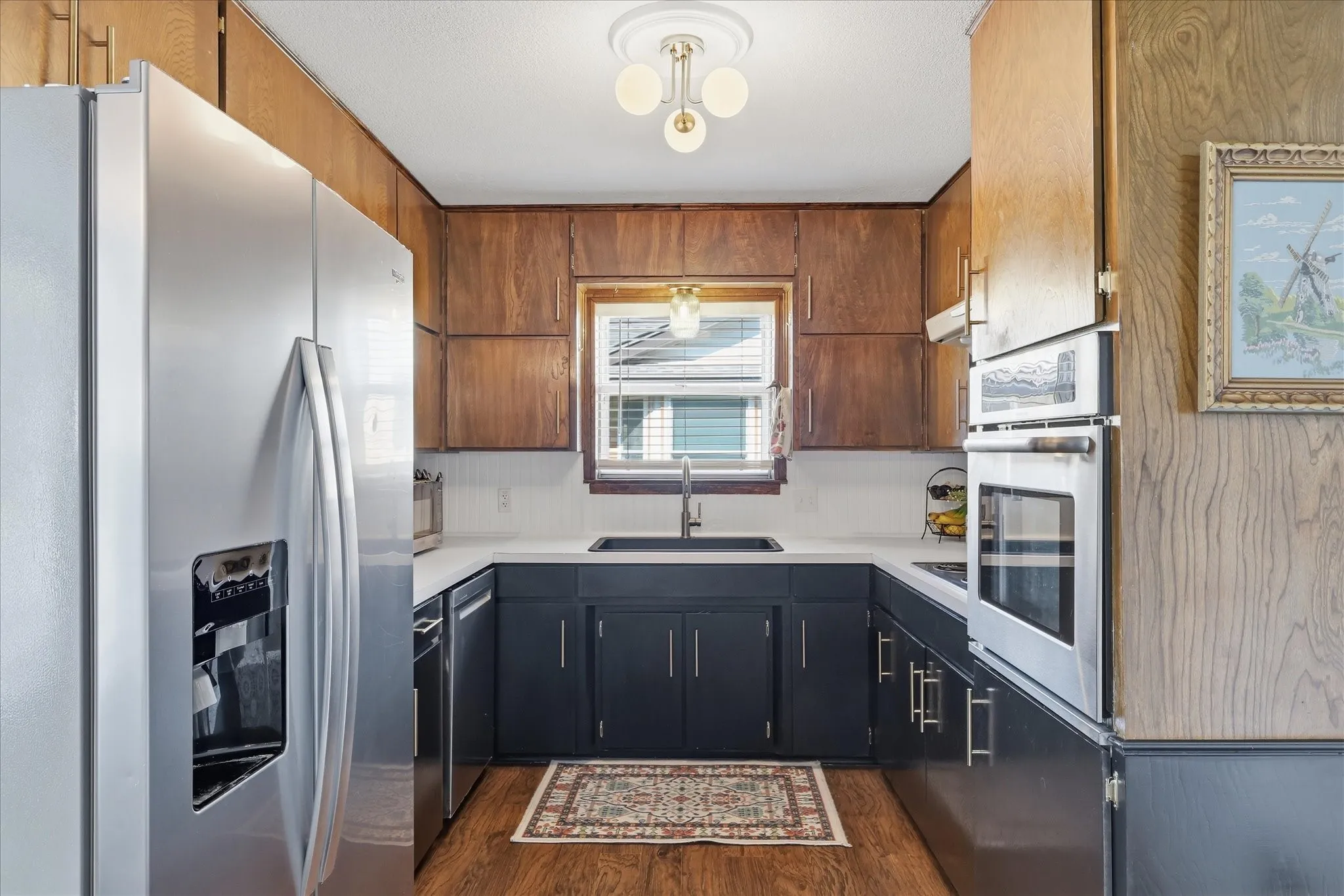 U-shaped kitchen featuring wood-finish flooring, white countertops, built-in stainless steel double ovens, and a stainless steel refrigerator