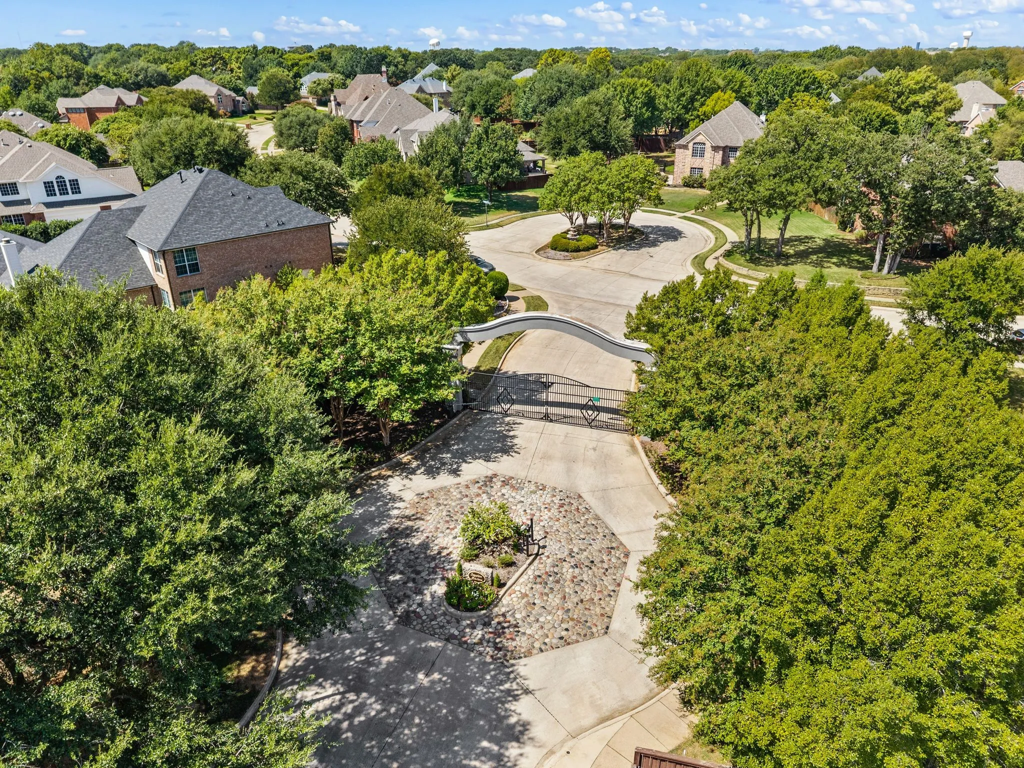 Gated entrance to Sapphire Enclave featuring mature trees and a manicured stone-finished island