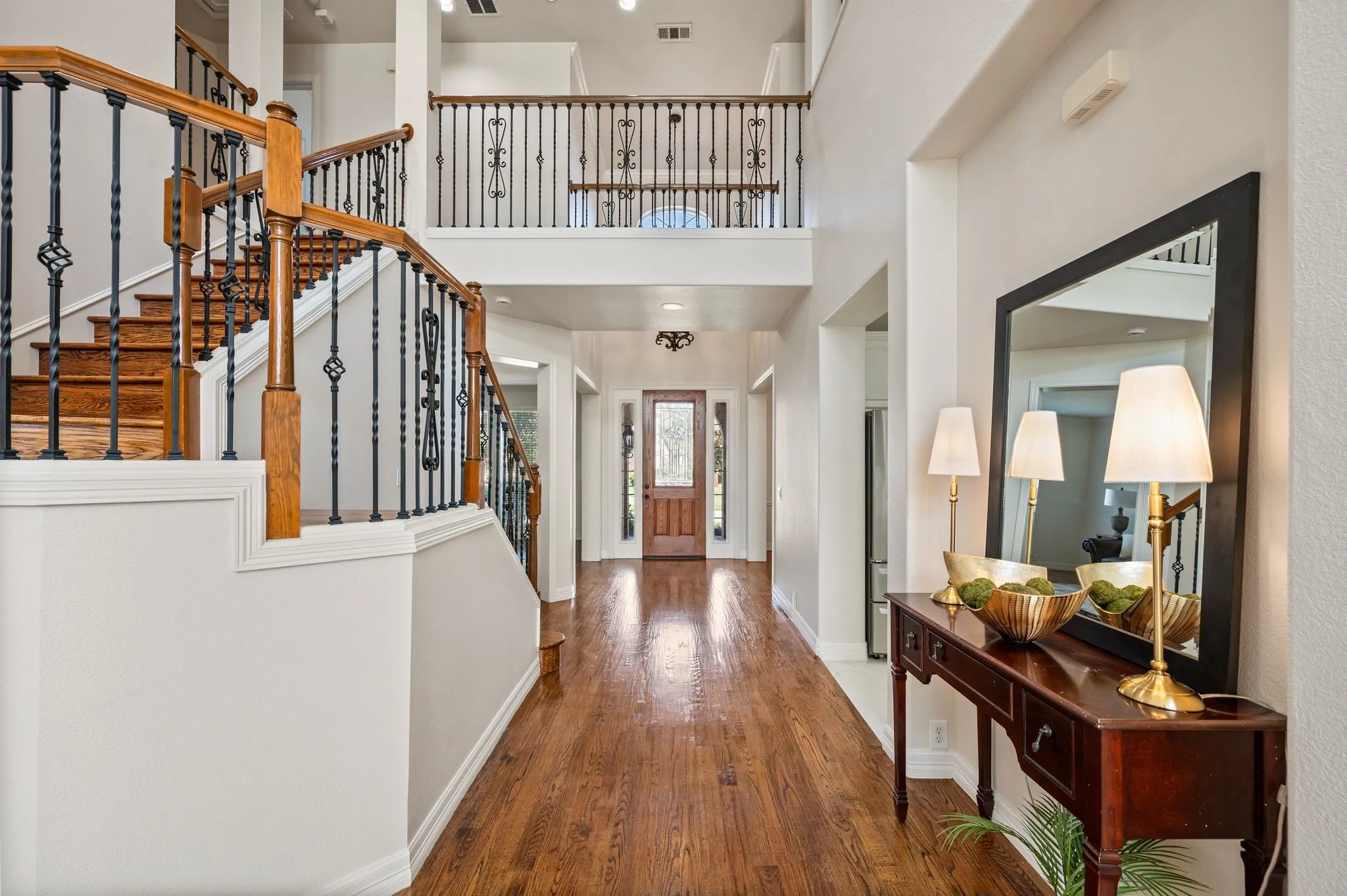 Two-story entry with wood-finish flooring, a grand staircase with wrought iron balusters and wood handrails, and a second-story landing