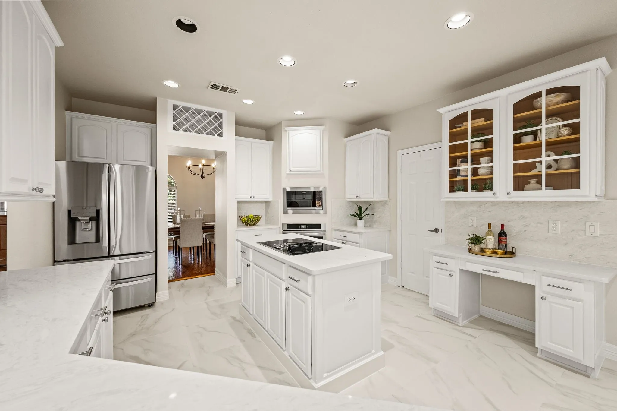White cabinetry, built-in stainless steel appliances, kitchen island with cooktop, white countertops, and light-toned tile flooring