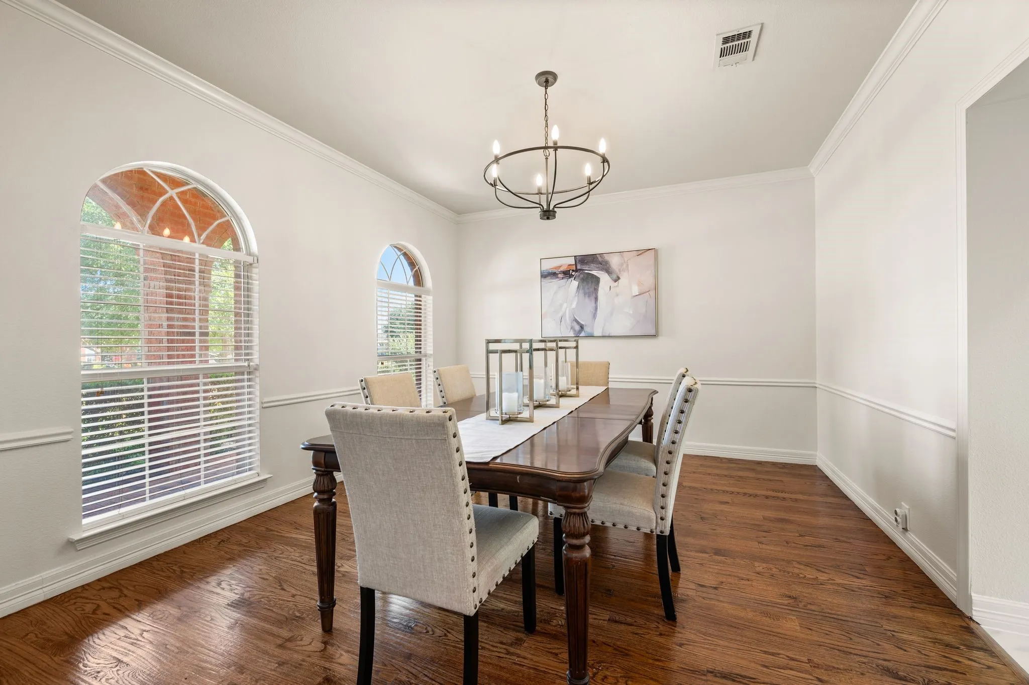 Hardwood-style flooring, arched windows, crown molding, chair rail molding, and a chandelier