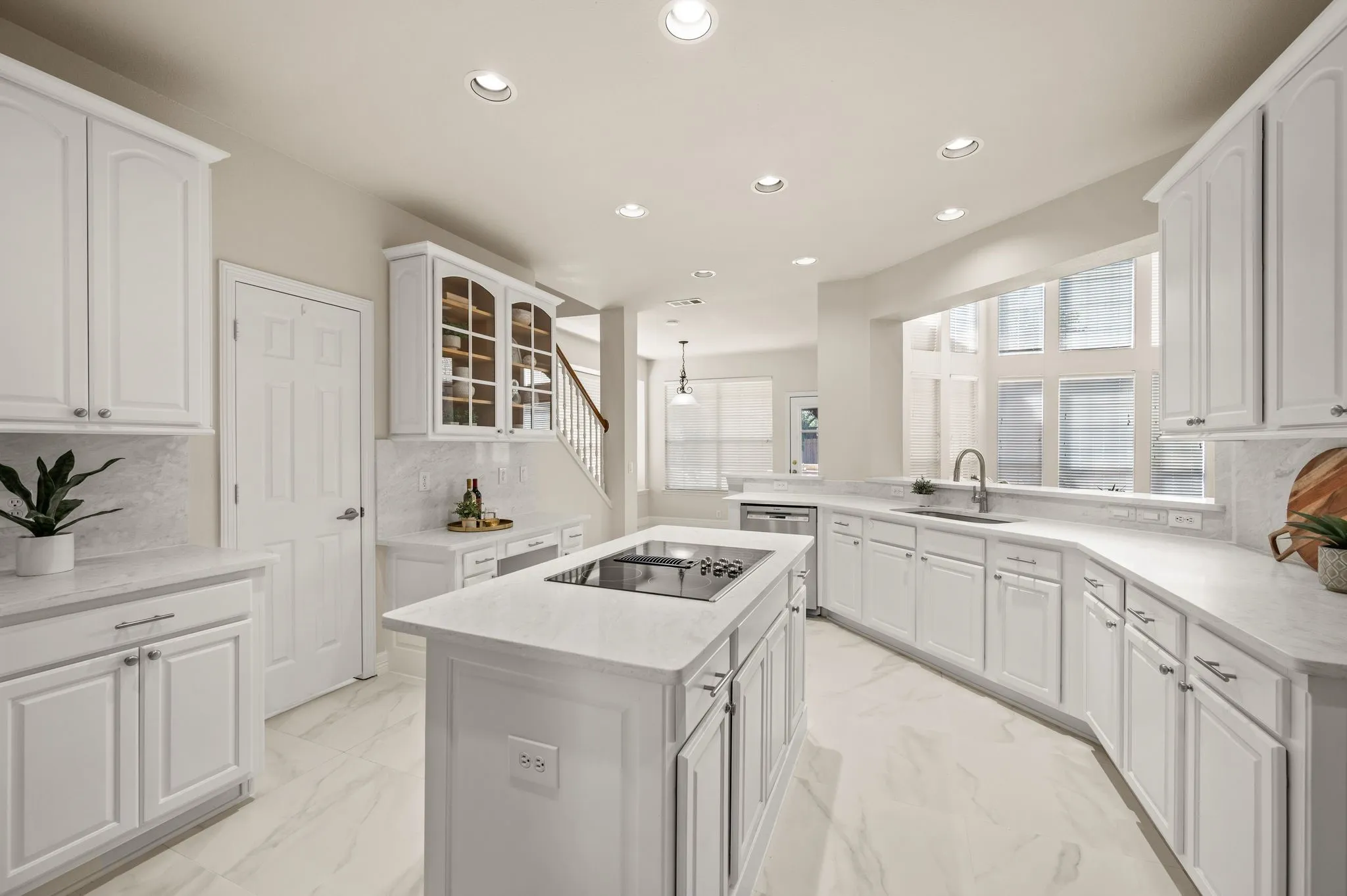 White cabinetry with brushed nickel hardware, built-in cooktop island, stone countertops, integrated sink with gooseneck faucet, and recessed lighting