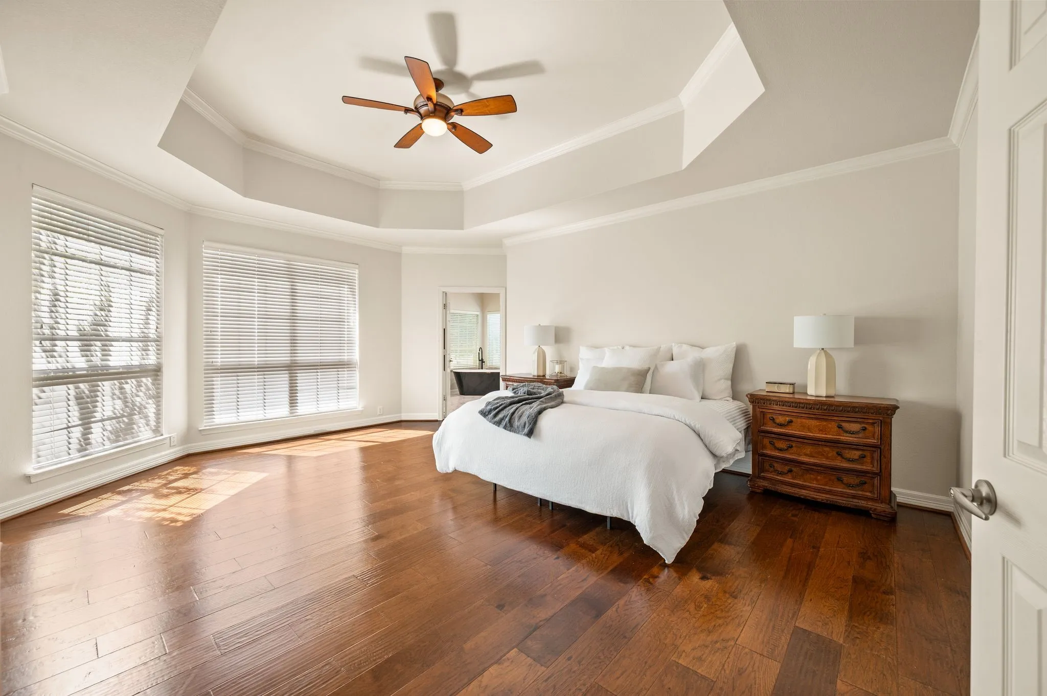 Hardwood flooring, recessed tray ceiling, ceiling fan, and multiple large windows with blinds